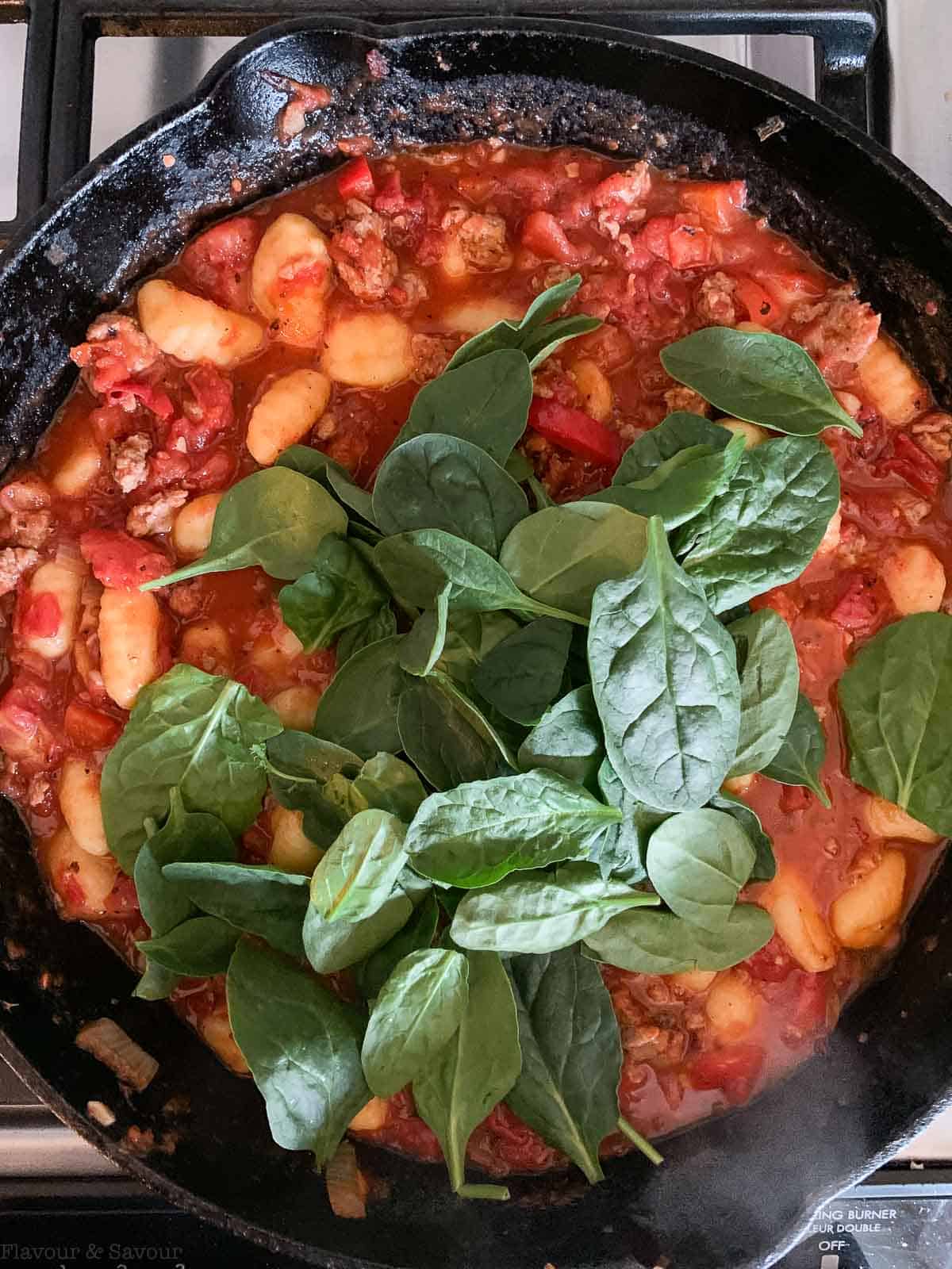 Fresh spinach leaves on tomato gnocchi bake in a skillet.