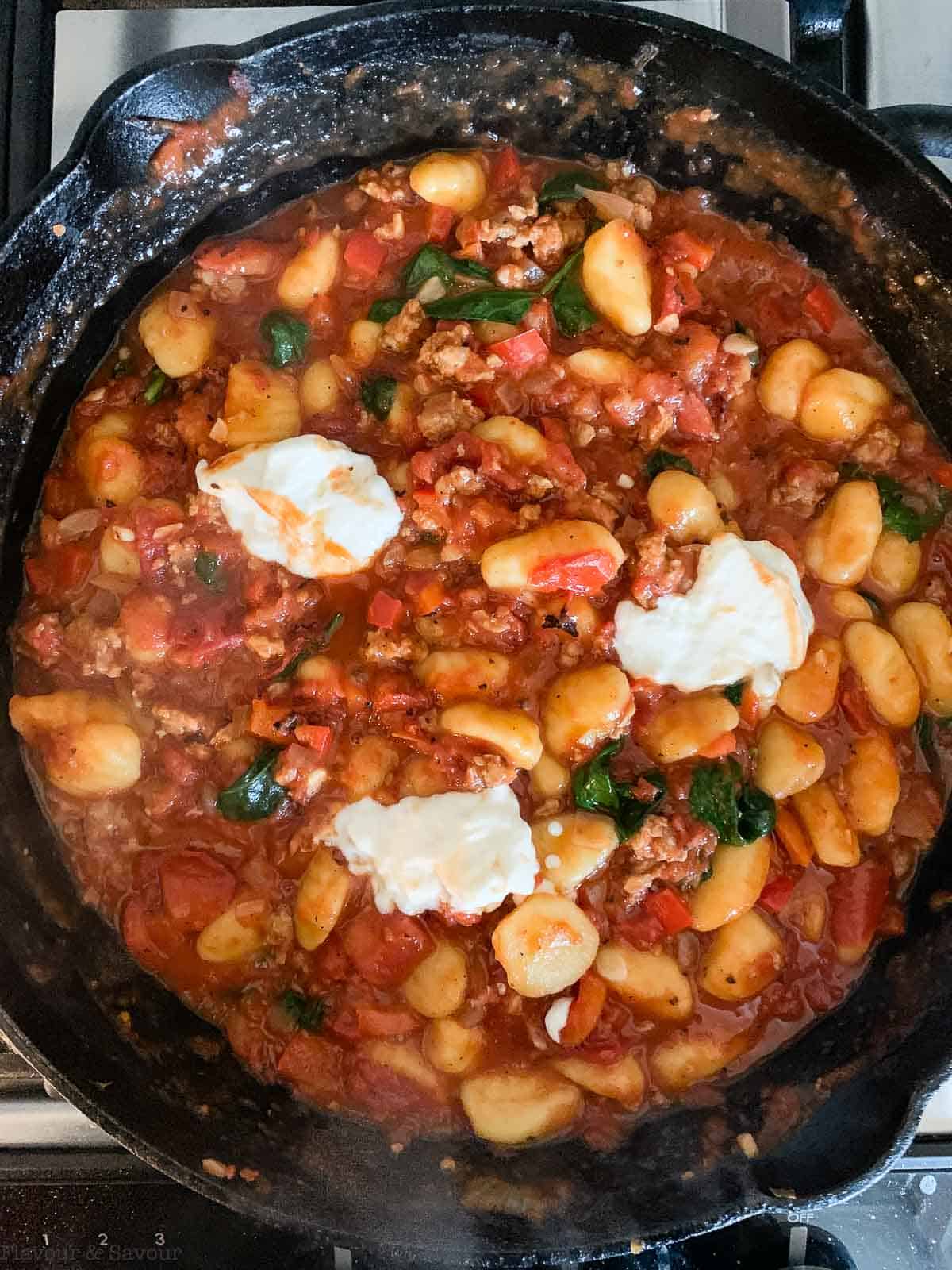 Spoonfuls of sour cream added to gnocchi bake in a skillet.