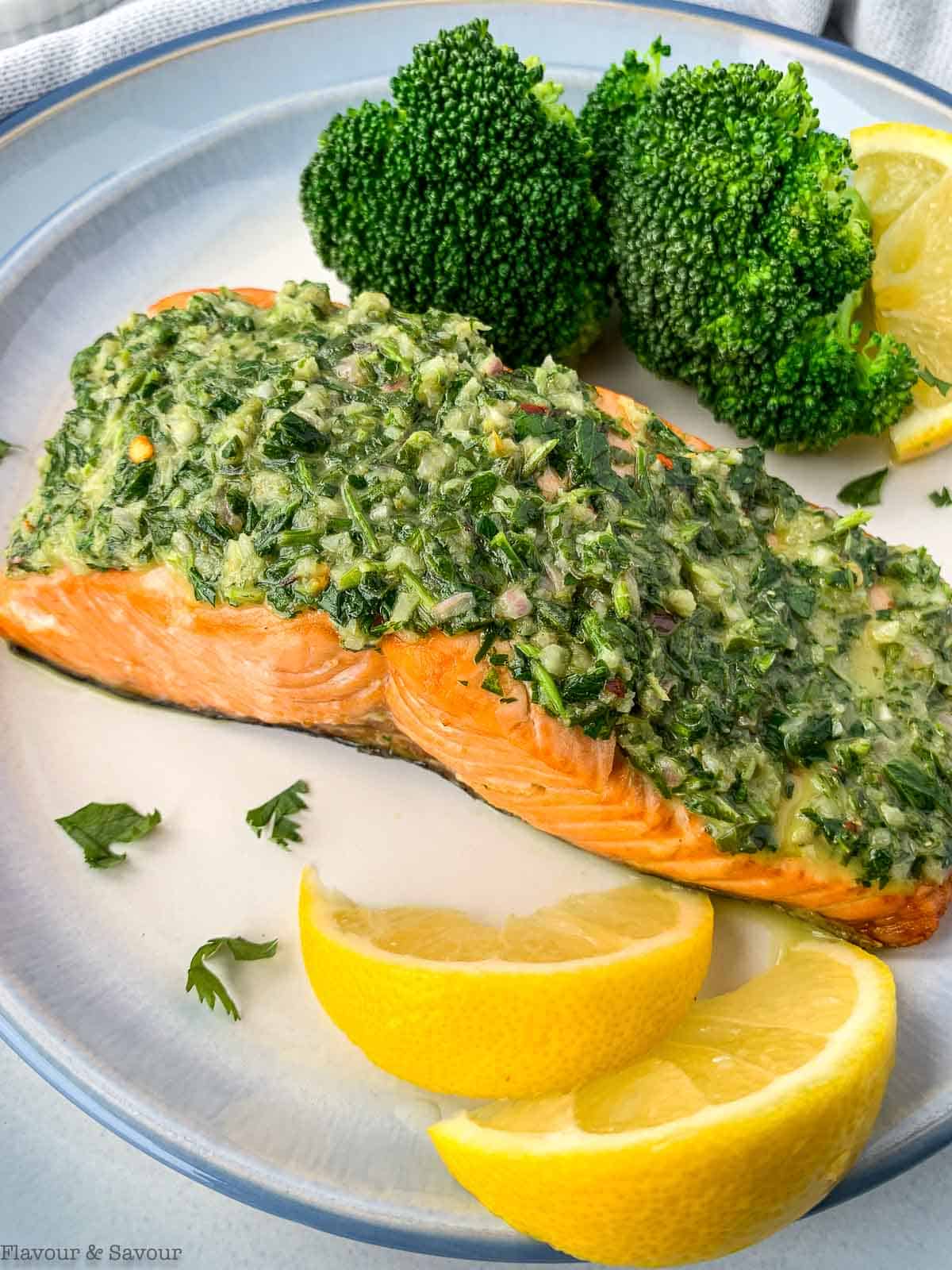 a filet of salmon with chimmichurri sauce with broccoli and lemon wedges