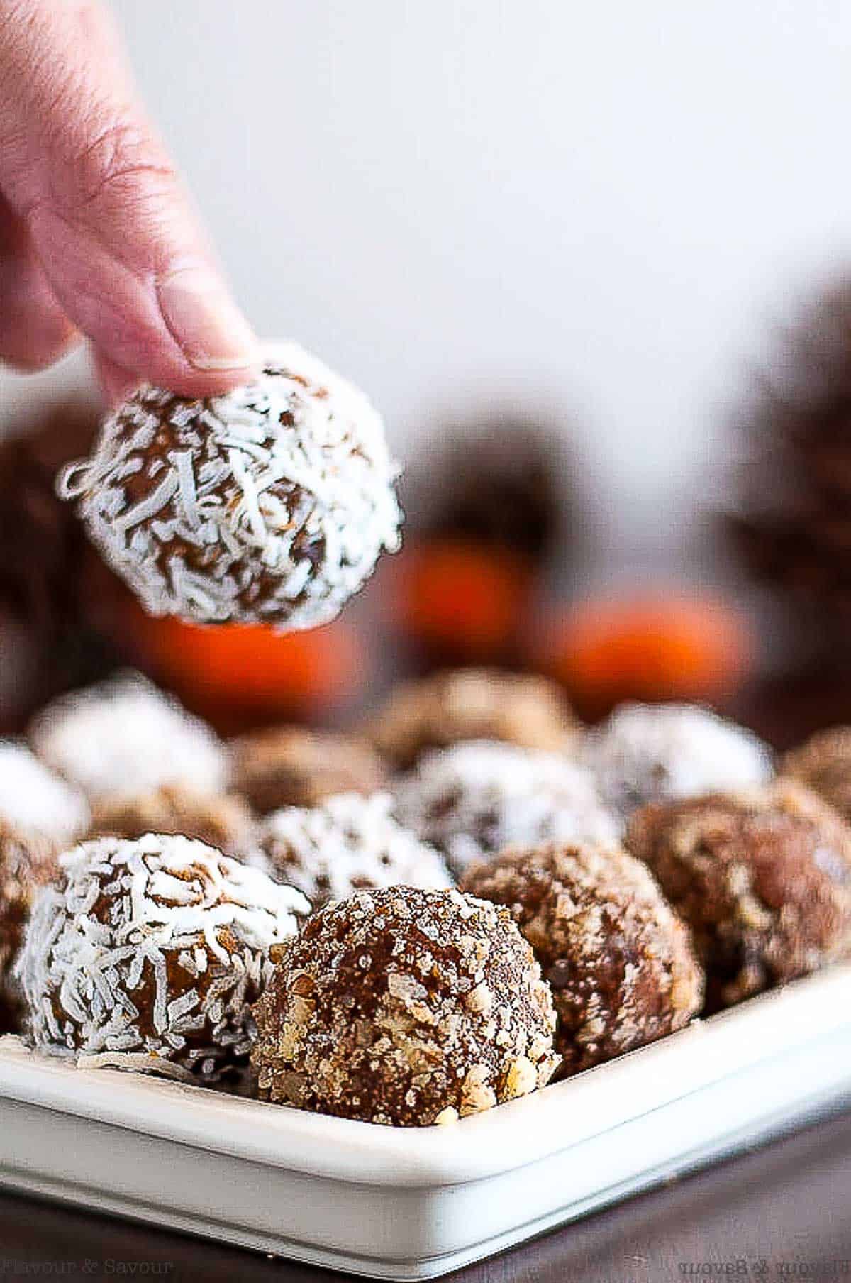 A hand lifting a peanut butter chocolate pumpkin energy ball from a plate.