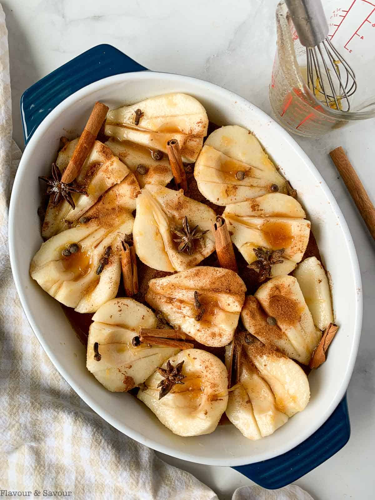 Pear halves in a baking dish covered with spices and poaching liquid.