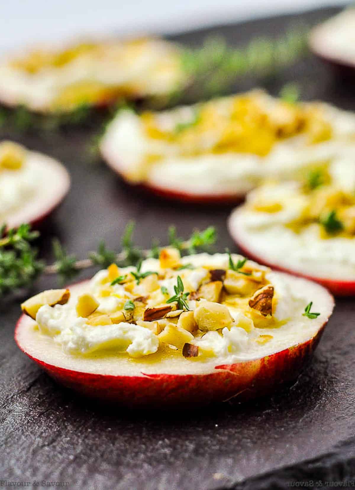 Whipped feta canapés on apple slices topped with hazelnuts on a black slate board.