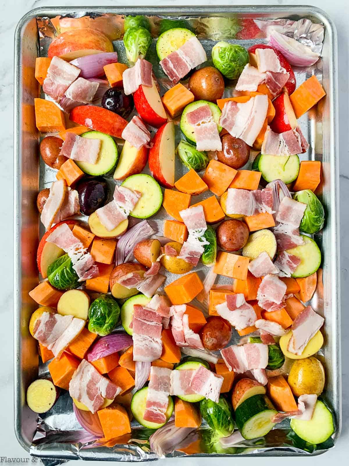 Raw vegetables with bacon on a sheet pan.