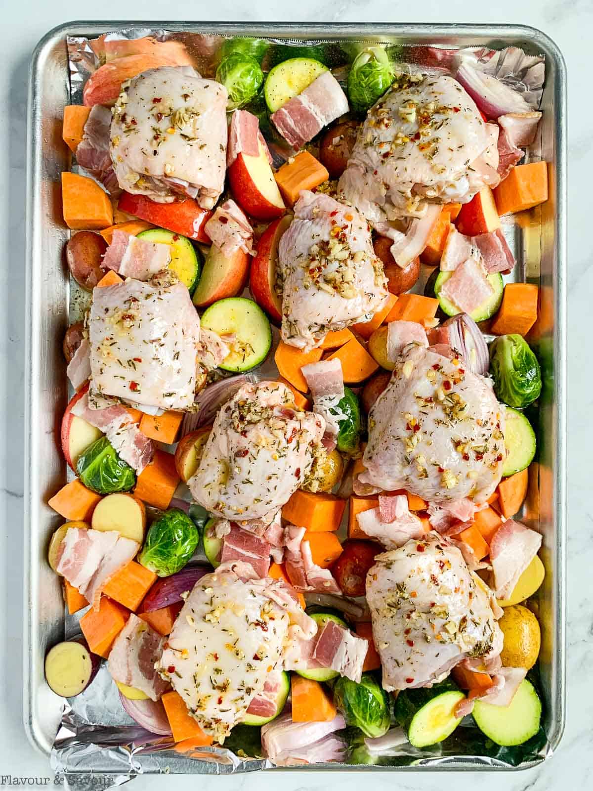 Raw vegetables with bacon and chicken thighs on a sheet pan.