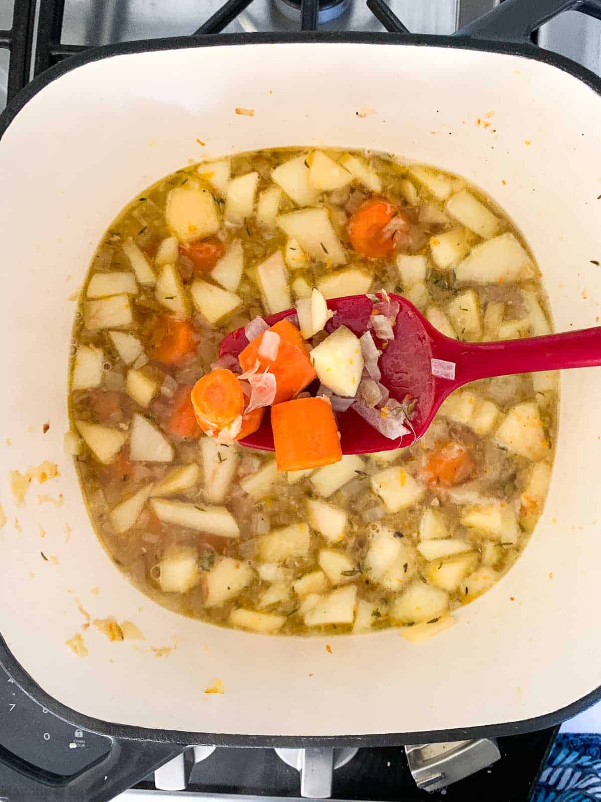 Adding roasted carrots to carrot ginger soup in a soup pot.