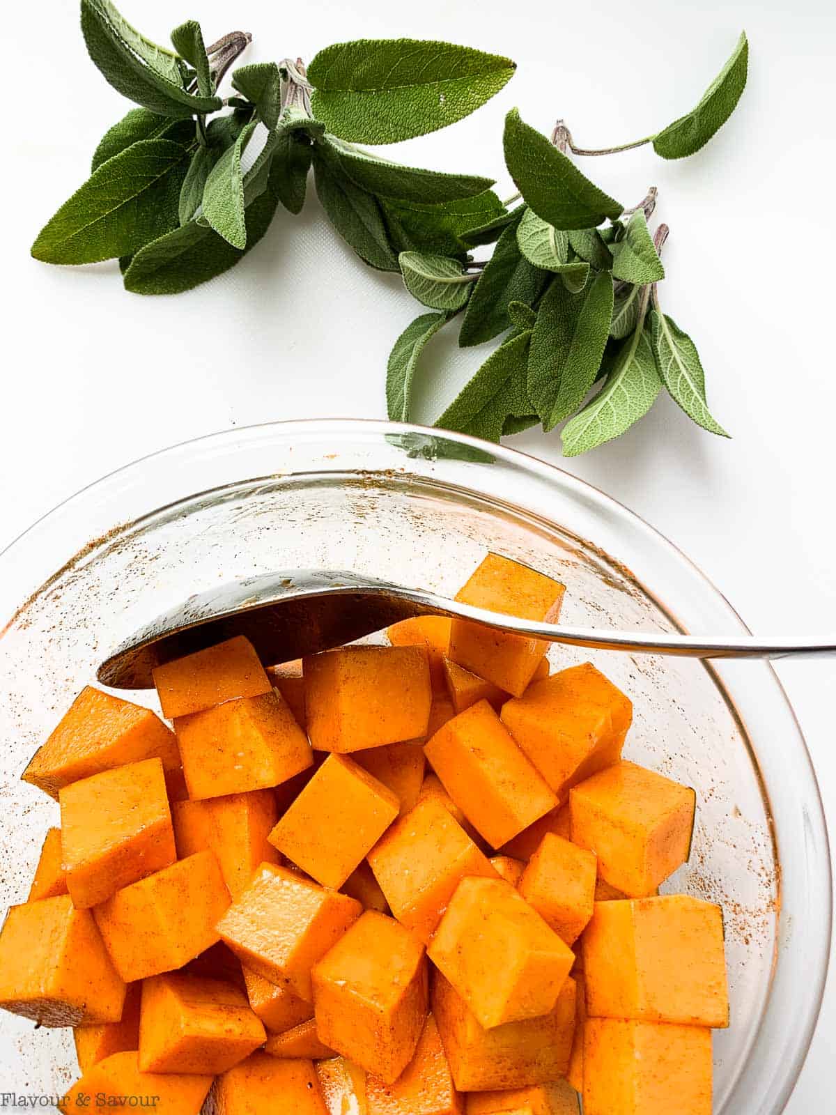 Butternut squash cubes in a bowl with fresh sage leaves beside.