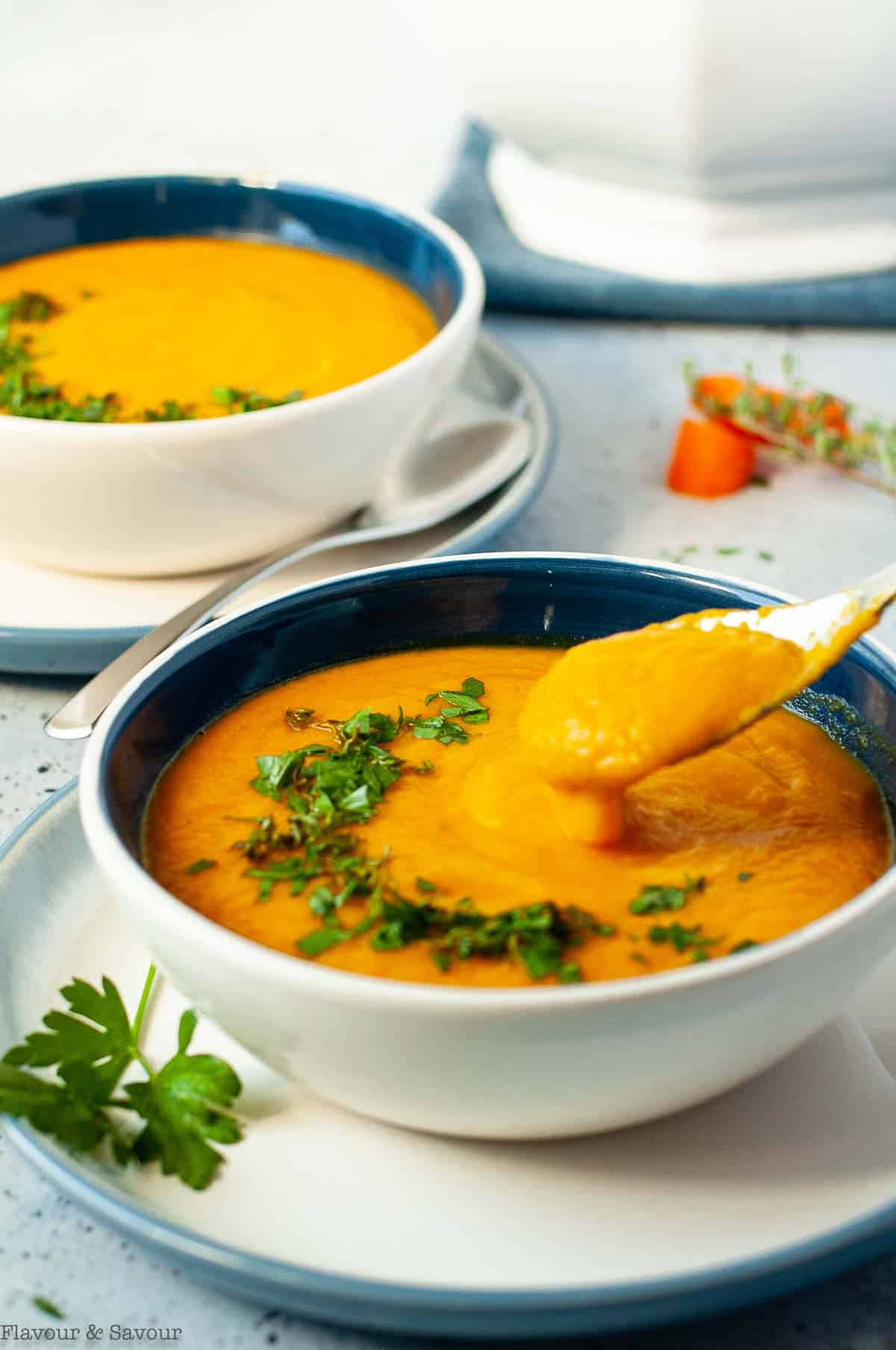 Two bowls of carrot ginger soup in blue bowls.