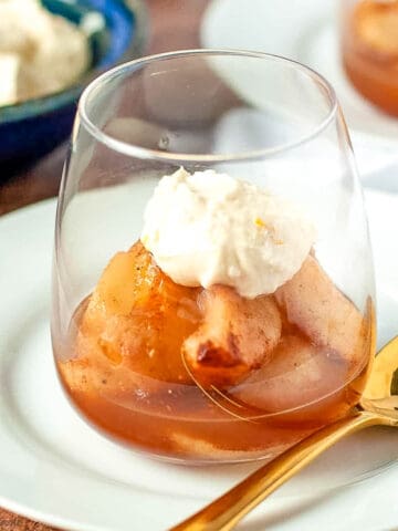 Poached cinnamon orange pears with maple mascarpone in a glass dessert dish with a spoon.