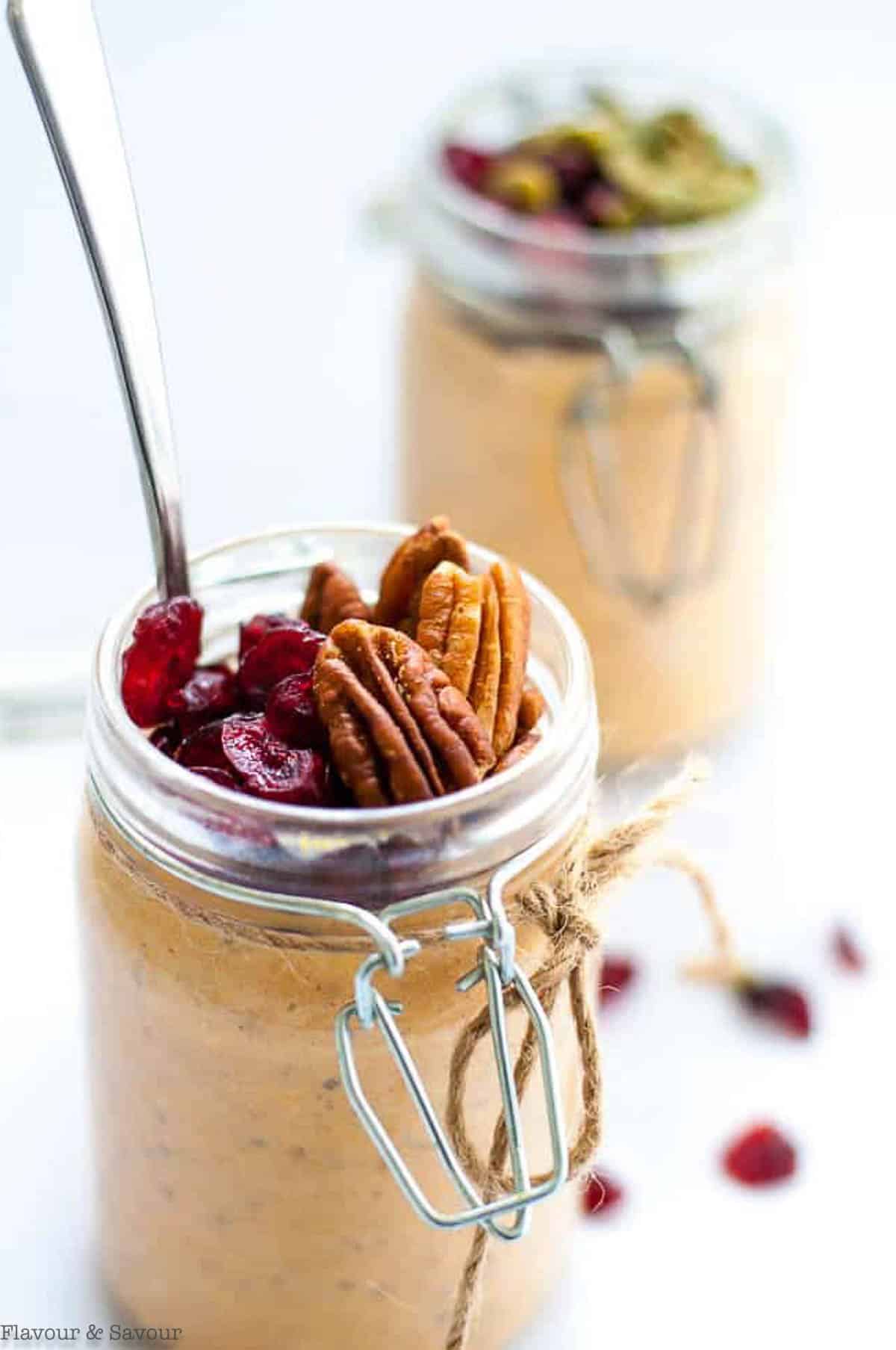 Creamy pumpkin pie overnight oats topped with pecans and cranberries with a spoon in the jar.