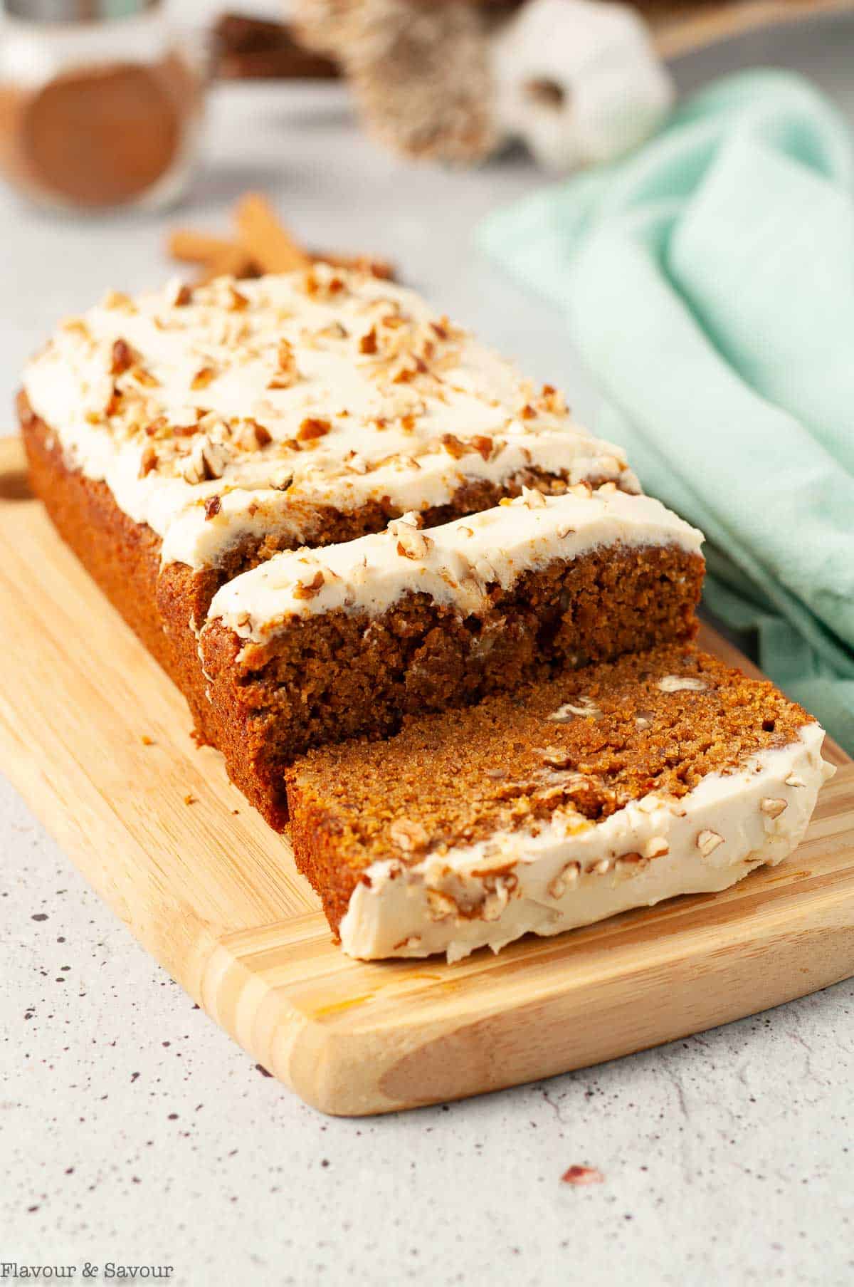 Slices of pumpkin bread with cream cheese frosting on a board.