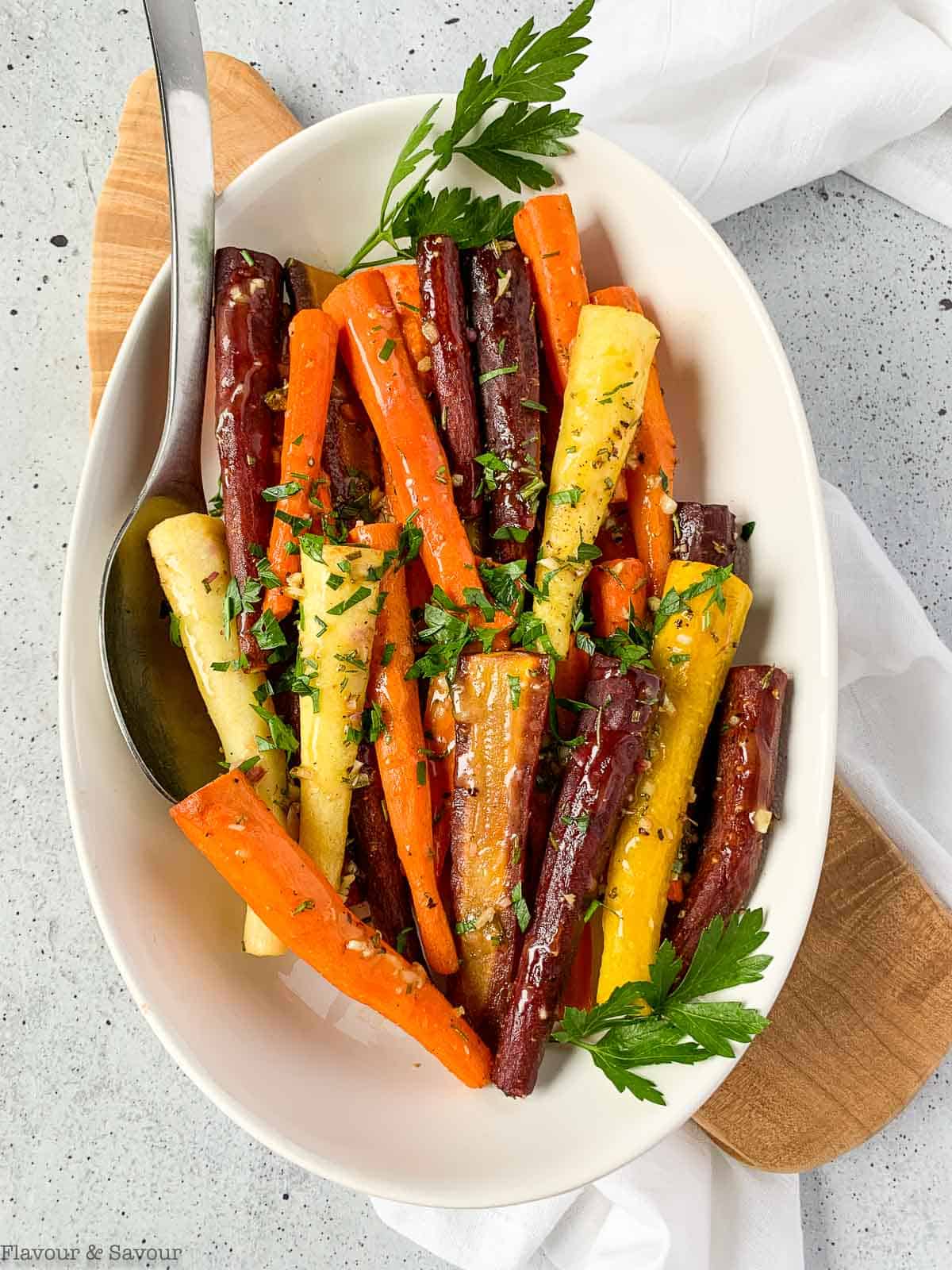 A serving bowl with honey-mustard glazed carrots and a spoon.