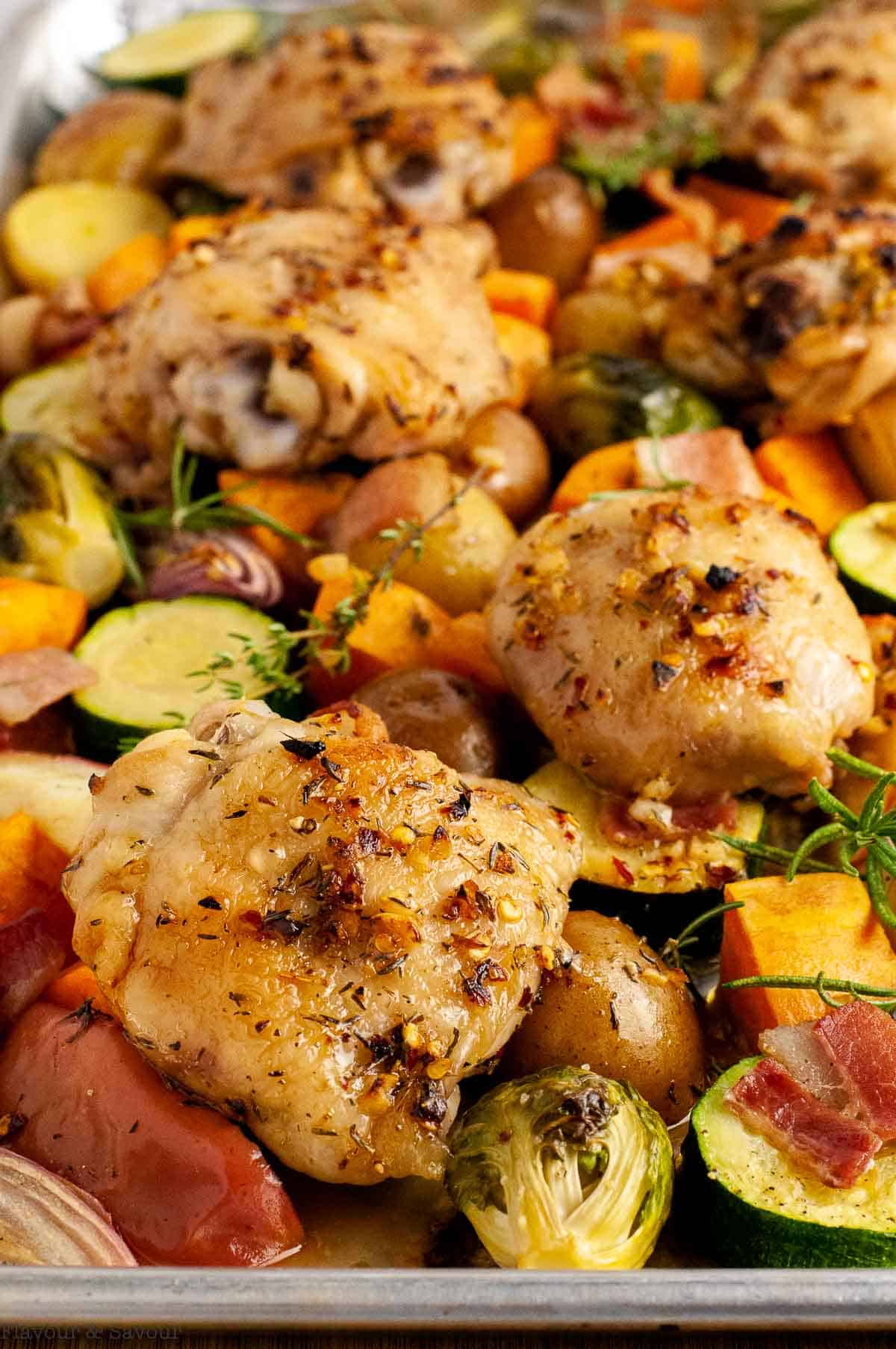 A sheet pan loaded with roasted chicken thighs, harvest vegetables, bacon and apples.