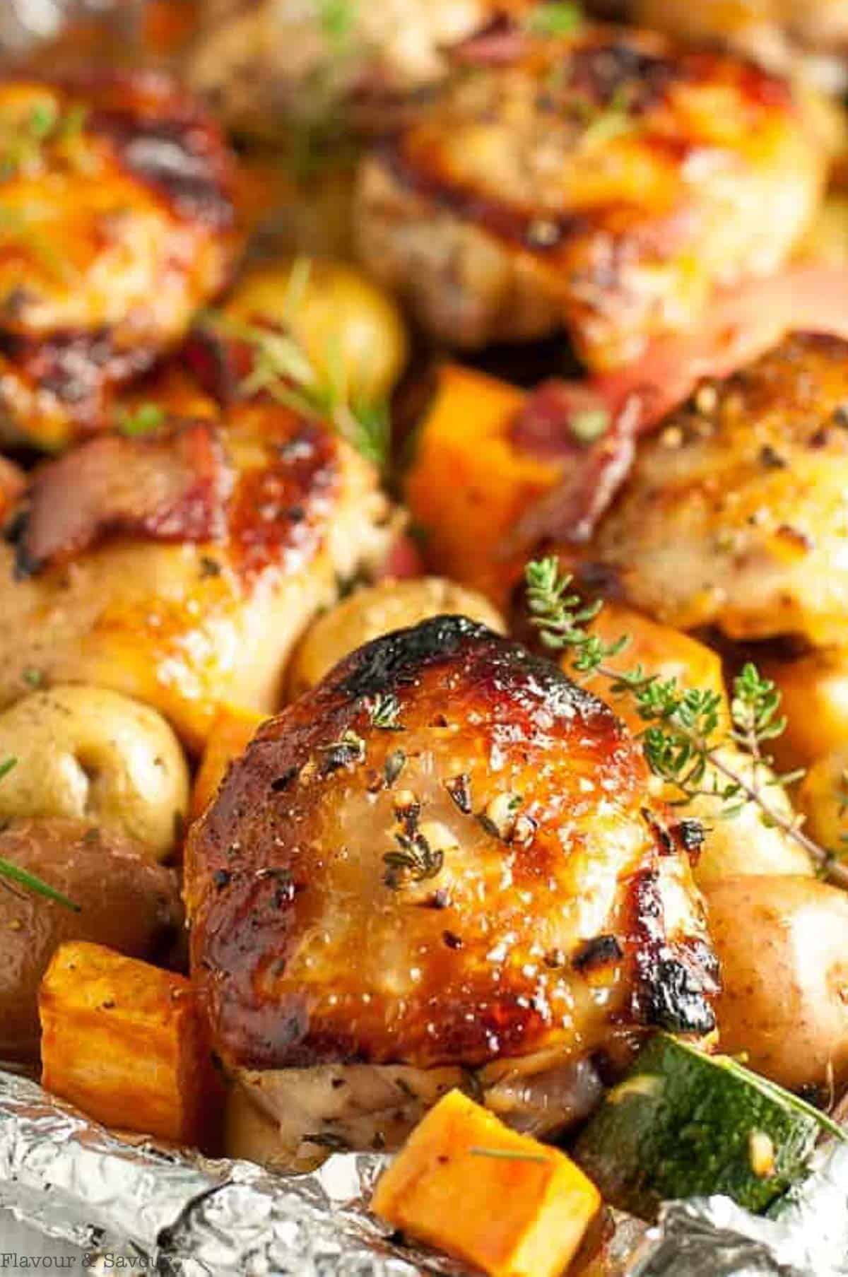 close up view of a roasted chicken thigh on a sheet pan with vegetables and herbs