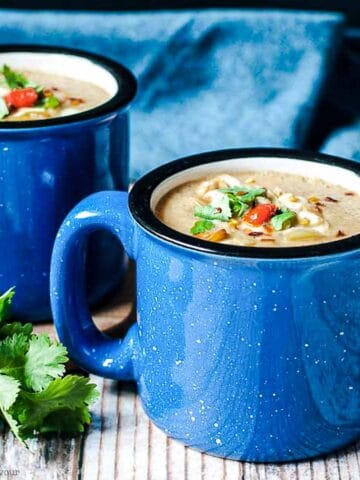 Close up view of two blue soup mugs with Moroccan Harissa Cauliflower Soup.