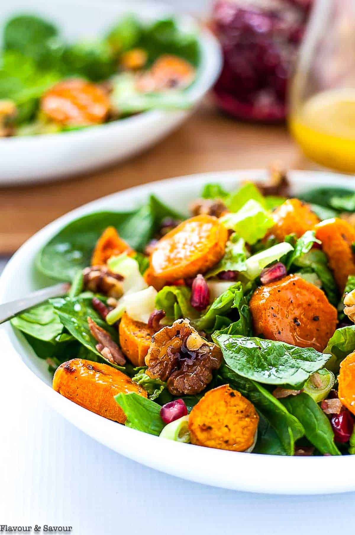 a bowl of spinach salad with roasted sweet potatoes, walnuts and pomegranate.