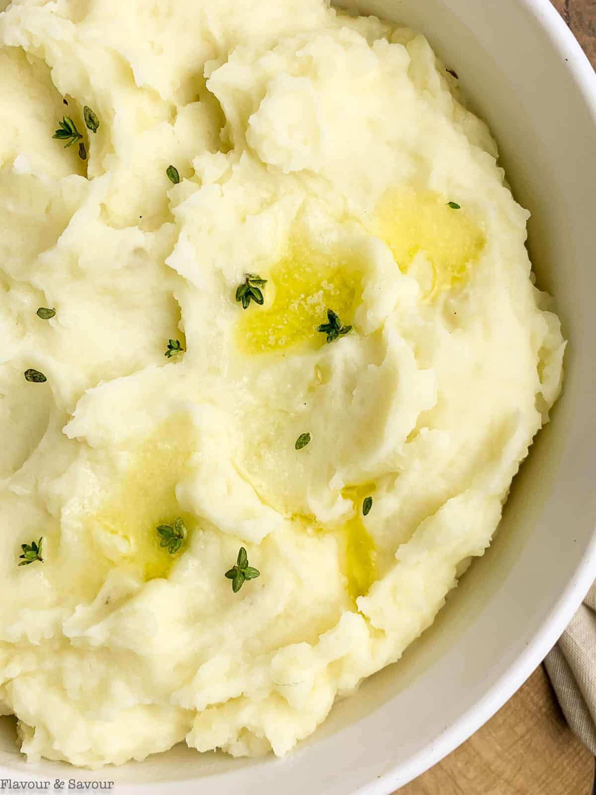 close up view of a bowl of garlic mashed potatoes with butter and fresh thyme