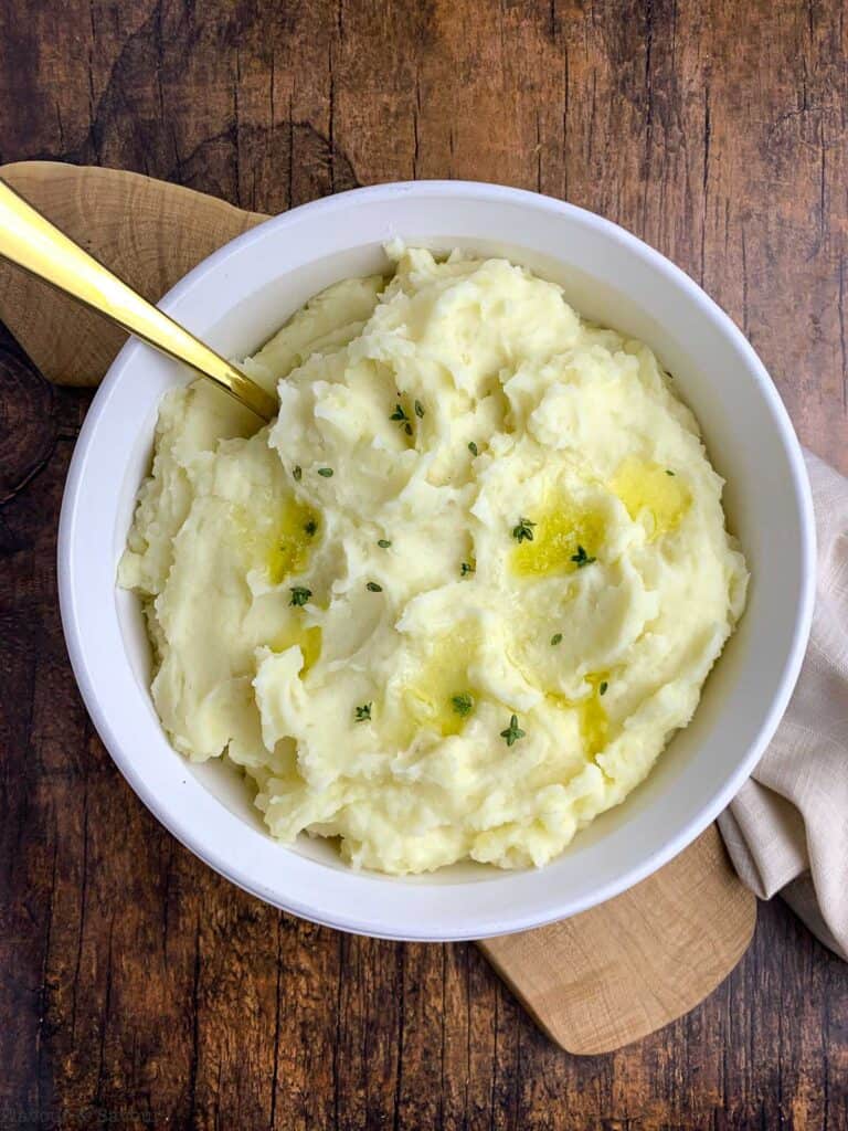 A bowl of mashed potatoes with melted butter and fresh thyme leaves