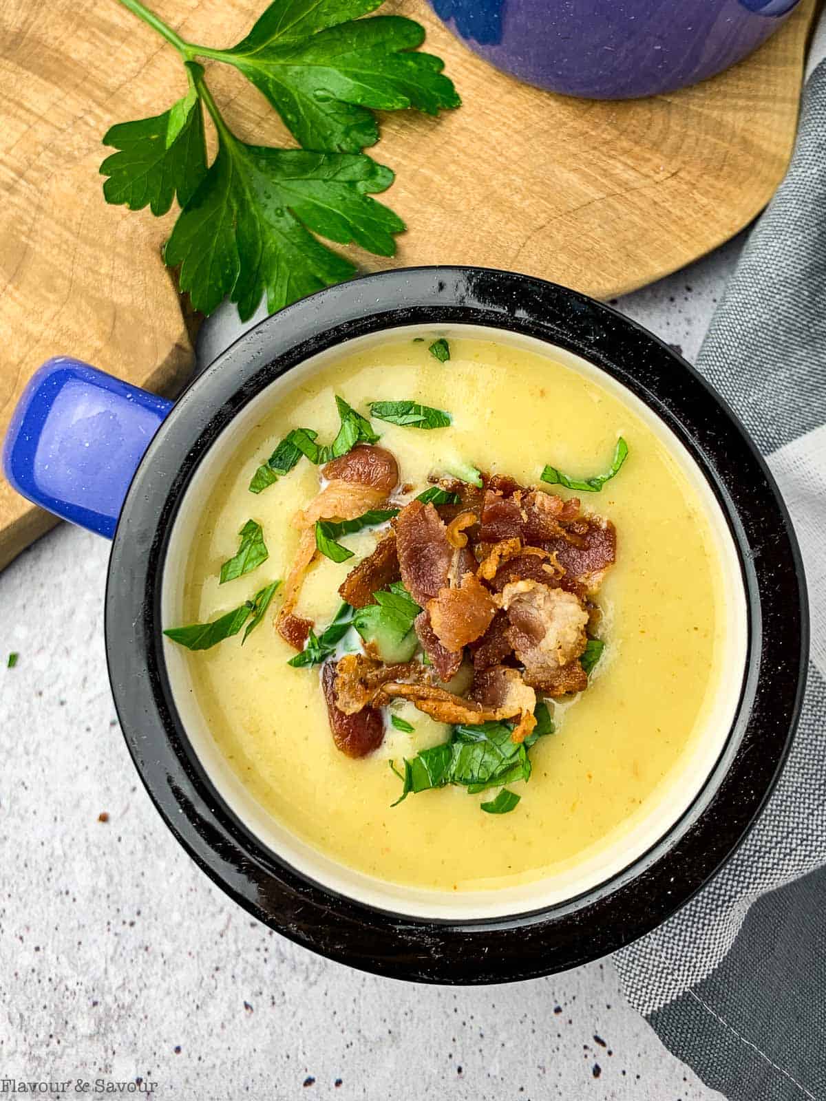 Overhead view of a mug of potato leek soup garnished with bacon bits and parsley.
