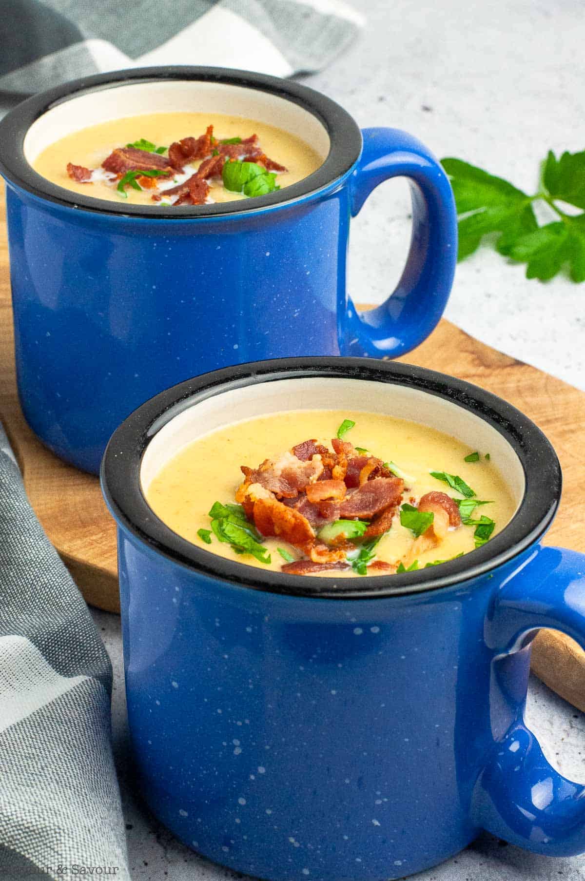 Two mugs of potato leek soup garnished with bacon.