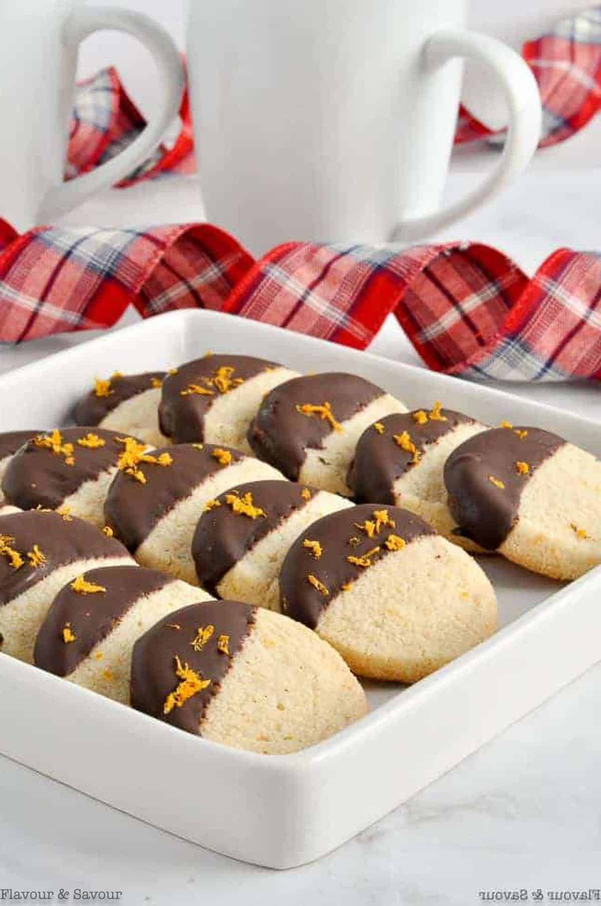 A white plate with almond flour shortbread cookies dipped in chocolate with orange zest.