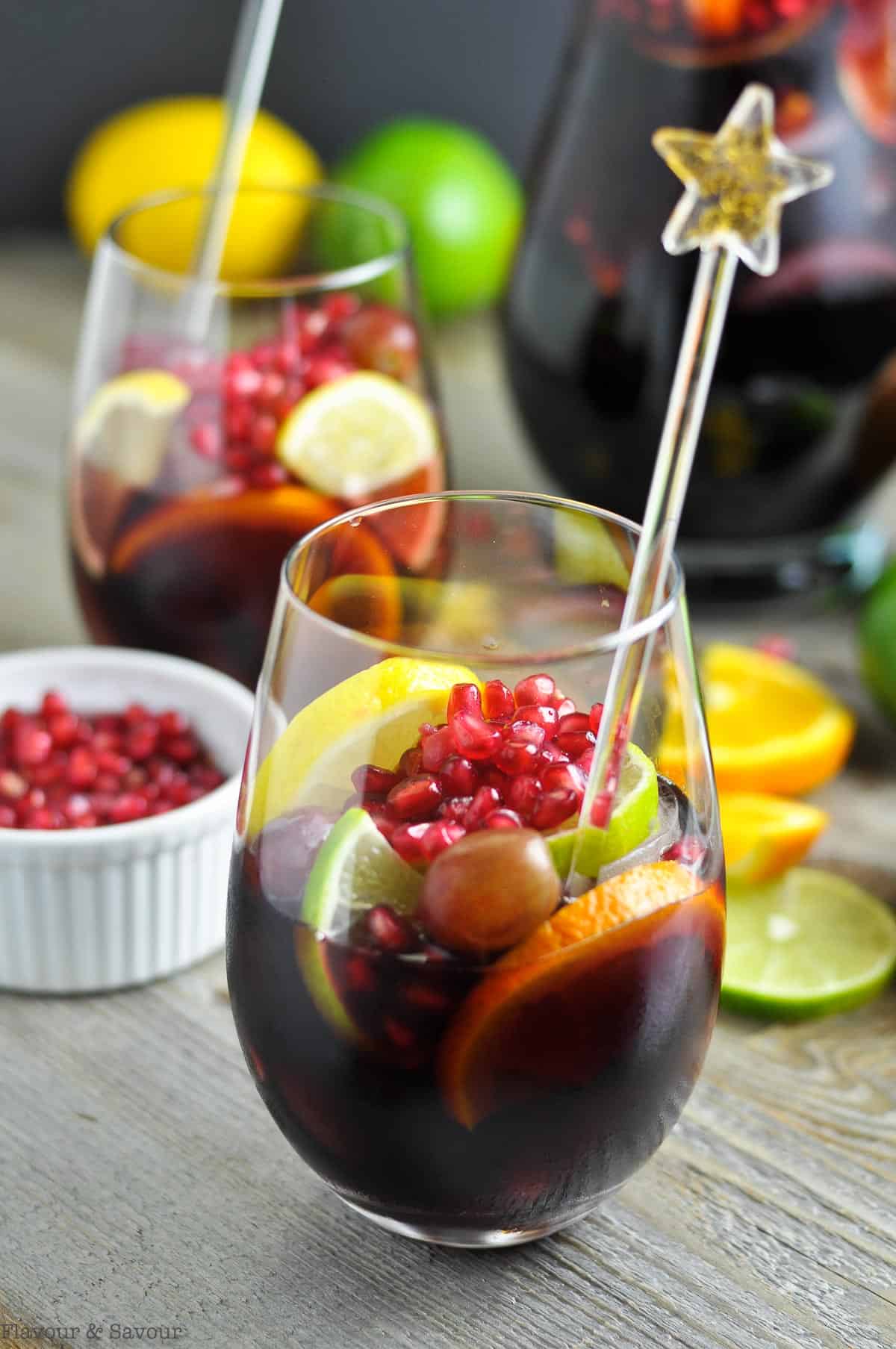 two glasses of pomegranate sangria with a pitcher in the background
