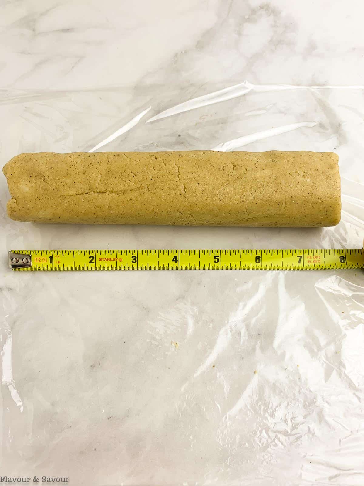 Cookie dough rolled into a log 8 inches long shown with measuring tape.
