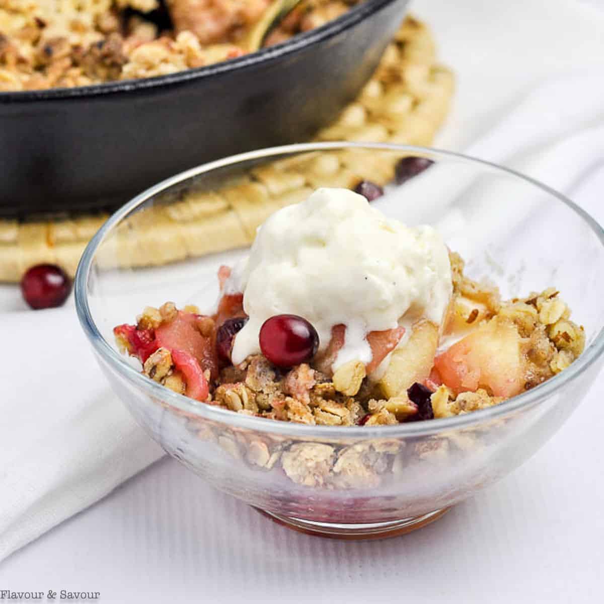 A glass dessert bowl with cranberry apple crisp and ice cream.