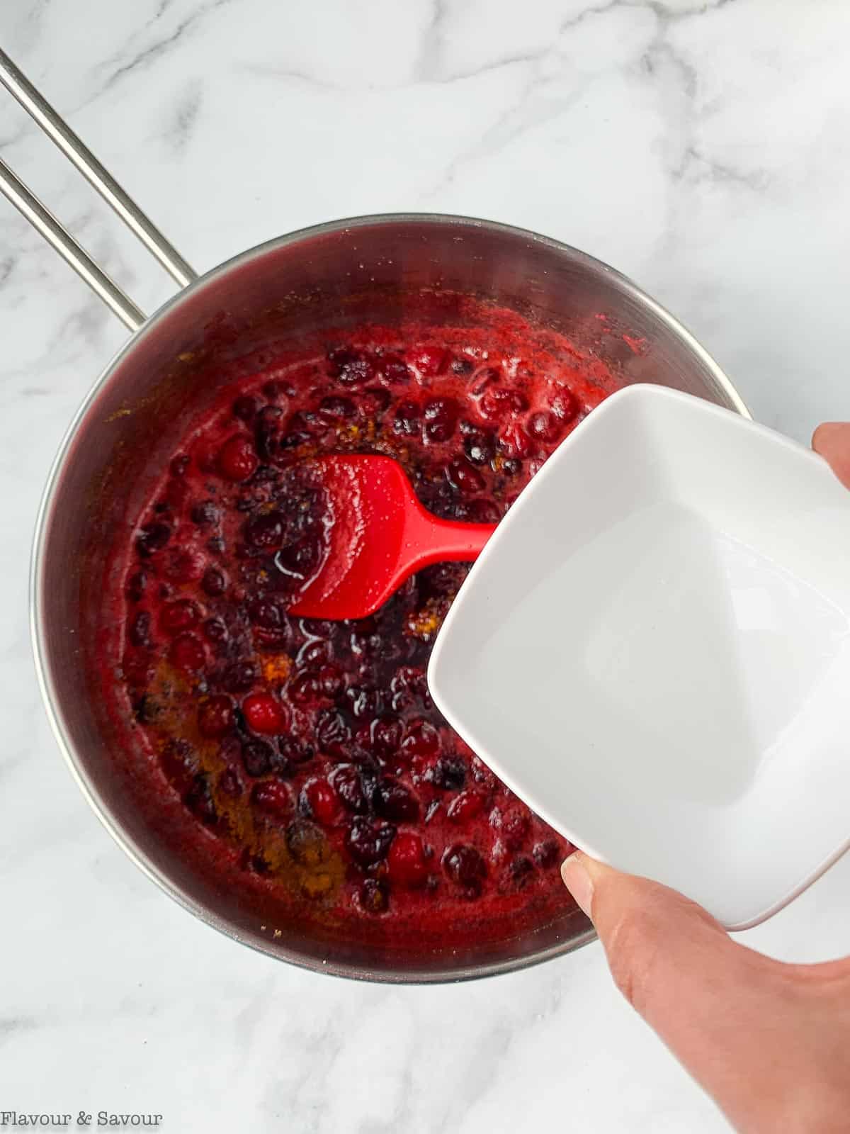 Adding orange liqueur to cranberry sauce in a saucepan.