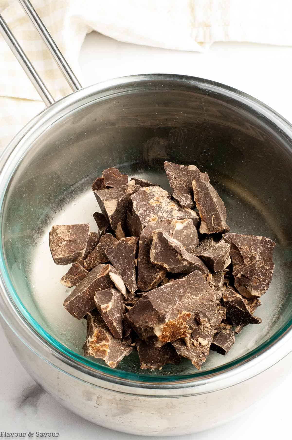 Chunks of dark chocolate in a glass bowl suspended over a saucepan of simmering water.