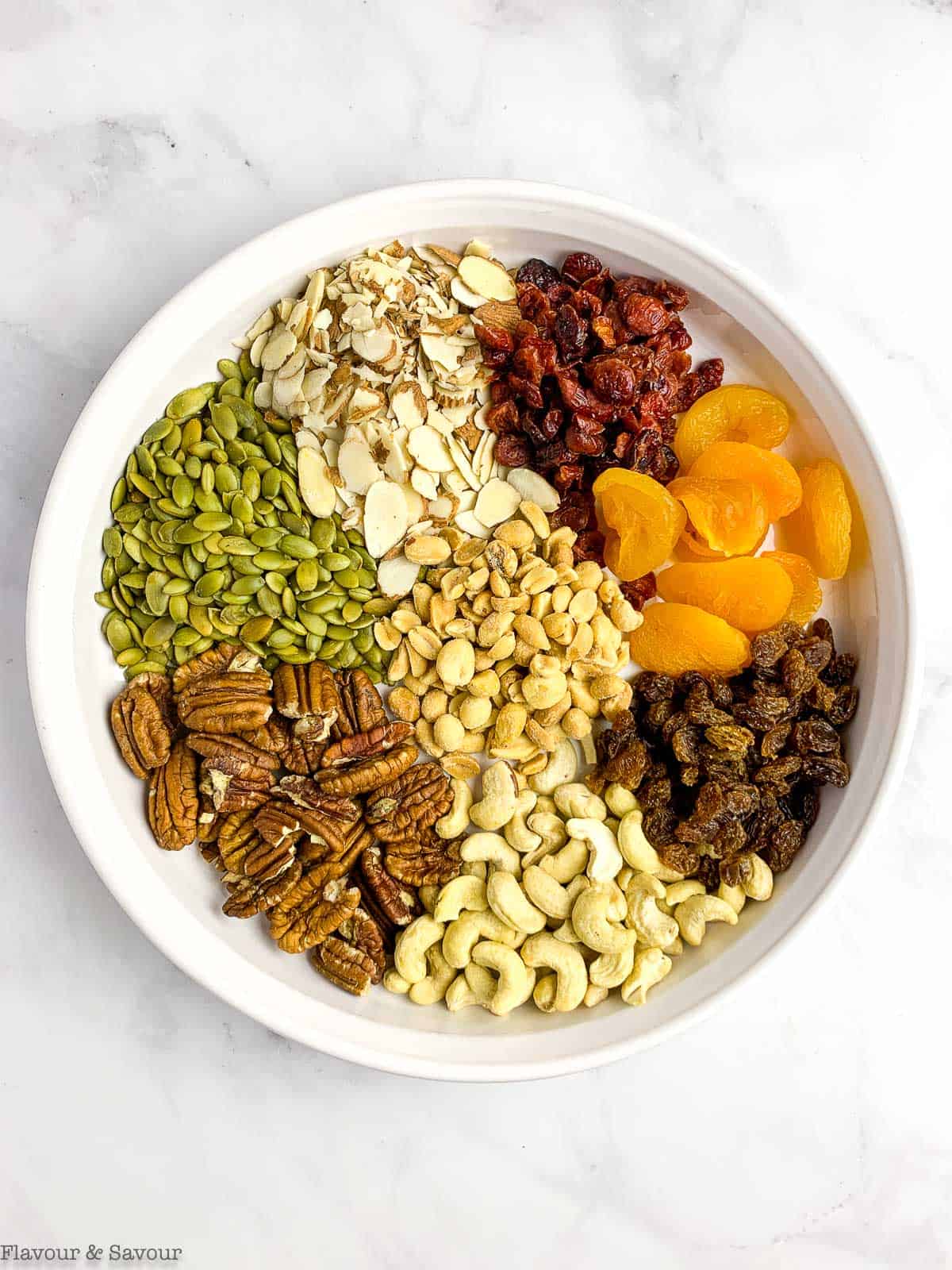 Nuts, seeds and dried fruit for trail mix chocolate nut clusters in a shallow bowl.