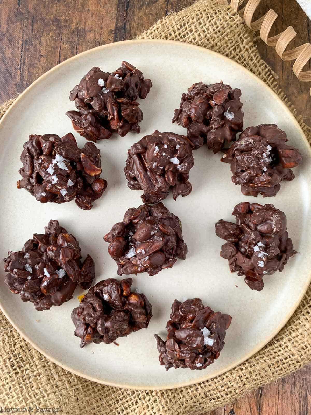 overhead view of chocolate nut clusters with nuts, seeds and dried fruit on a plate