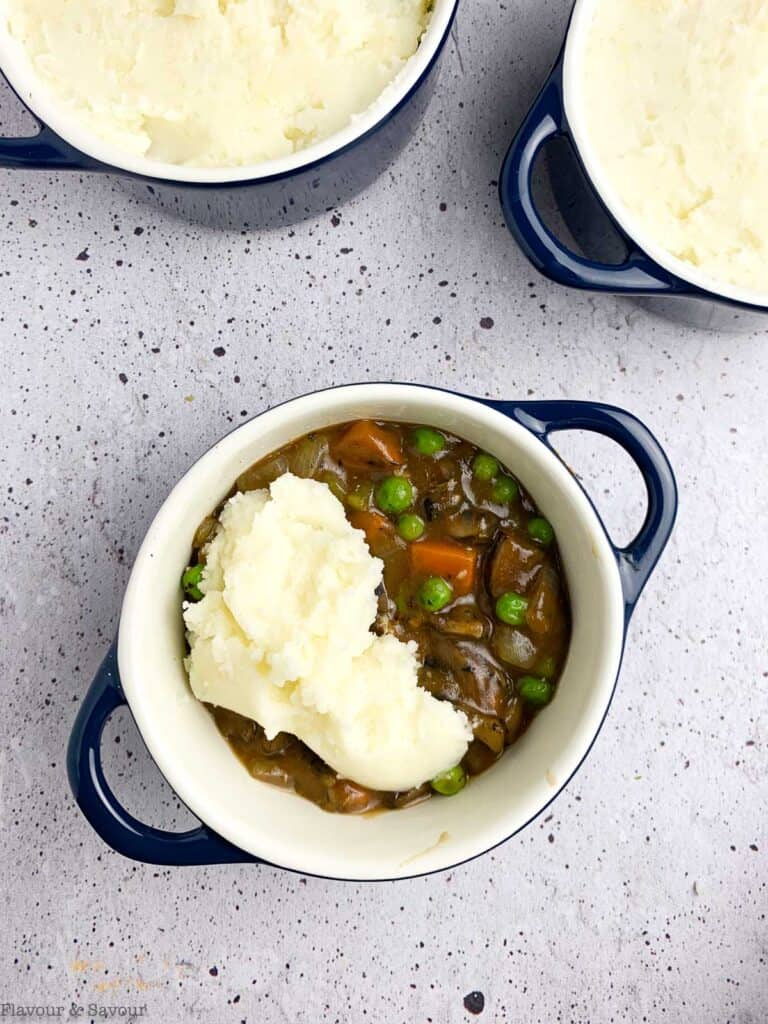 Adding mashed potatoes to individual shepherd's pies.