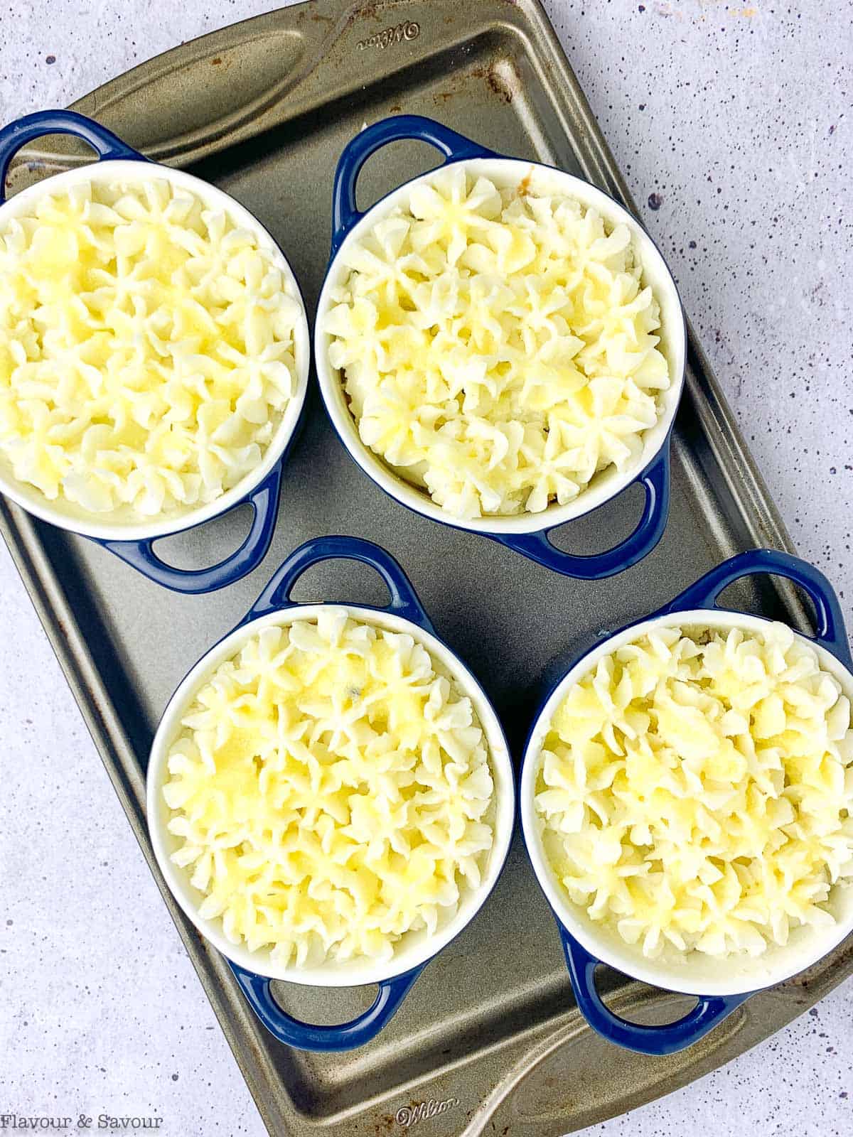 Individual shepherd's pies ready for the oven with piped mashed potato topping.