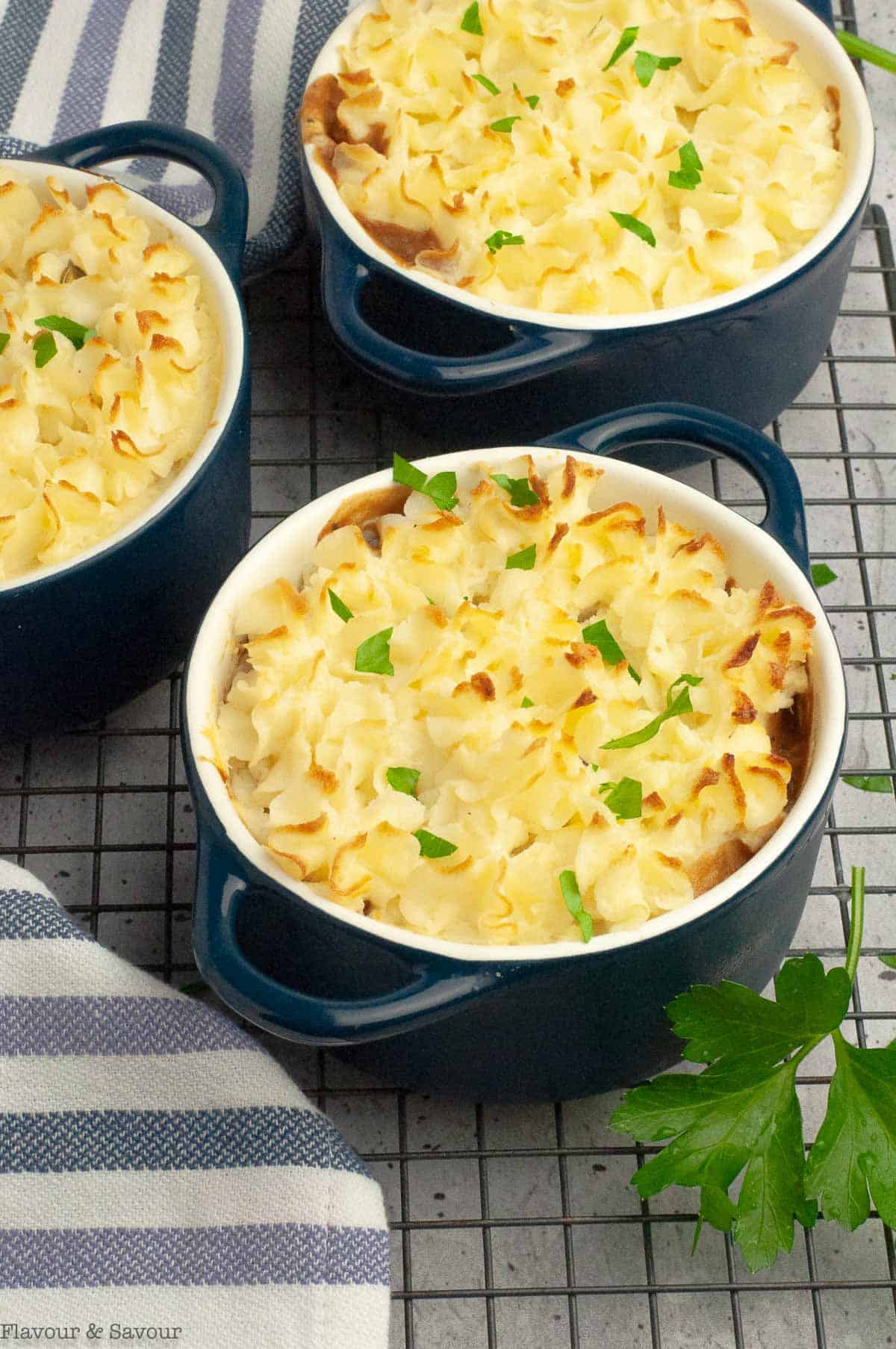 Mini vegetarian shepherd's pies with mushrooms in casserole dishes on a cooling rack.