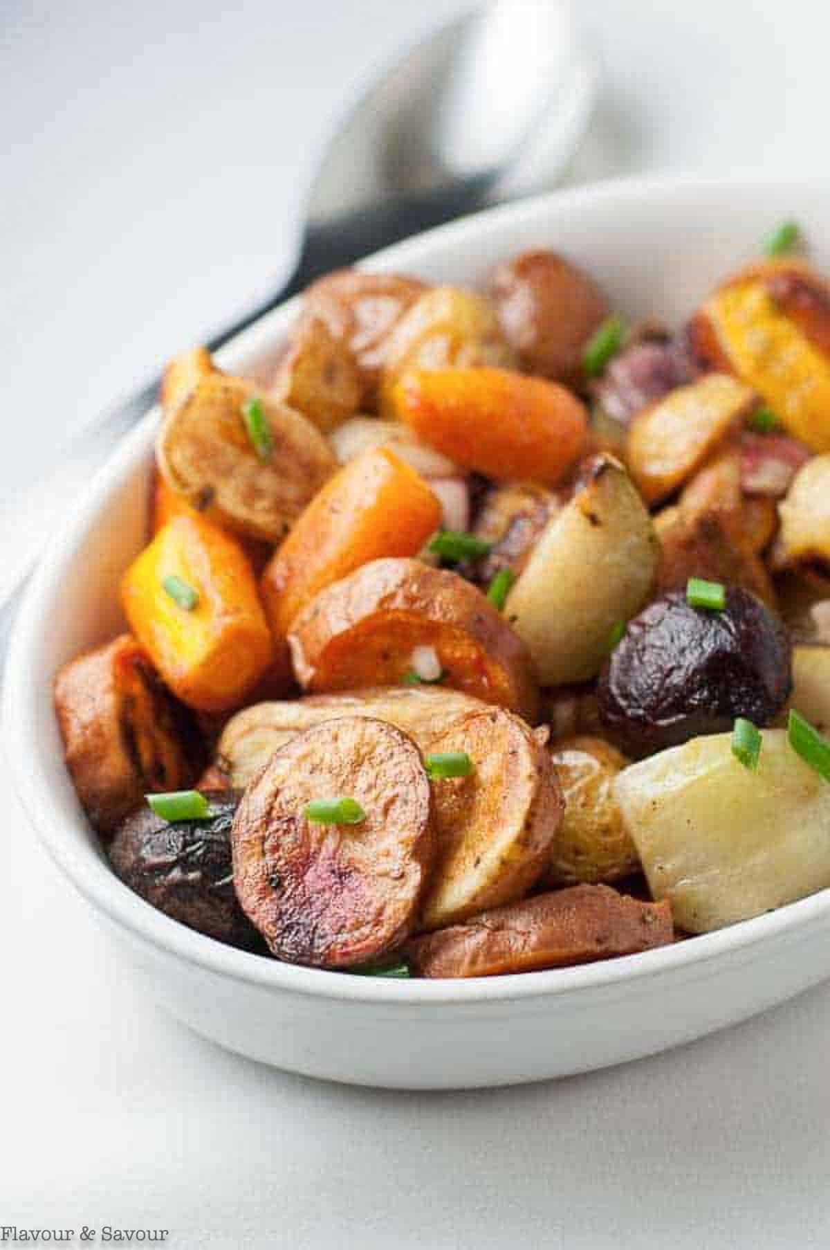 apple cider roasted root vegetables in an oval dish with a serving spoon.