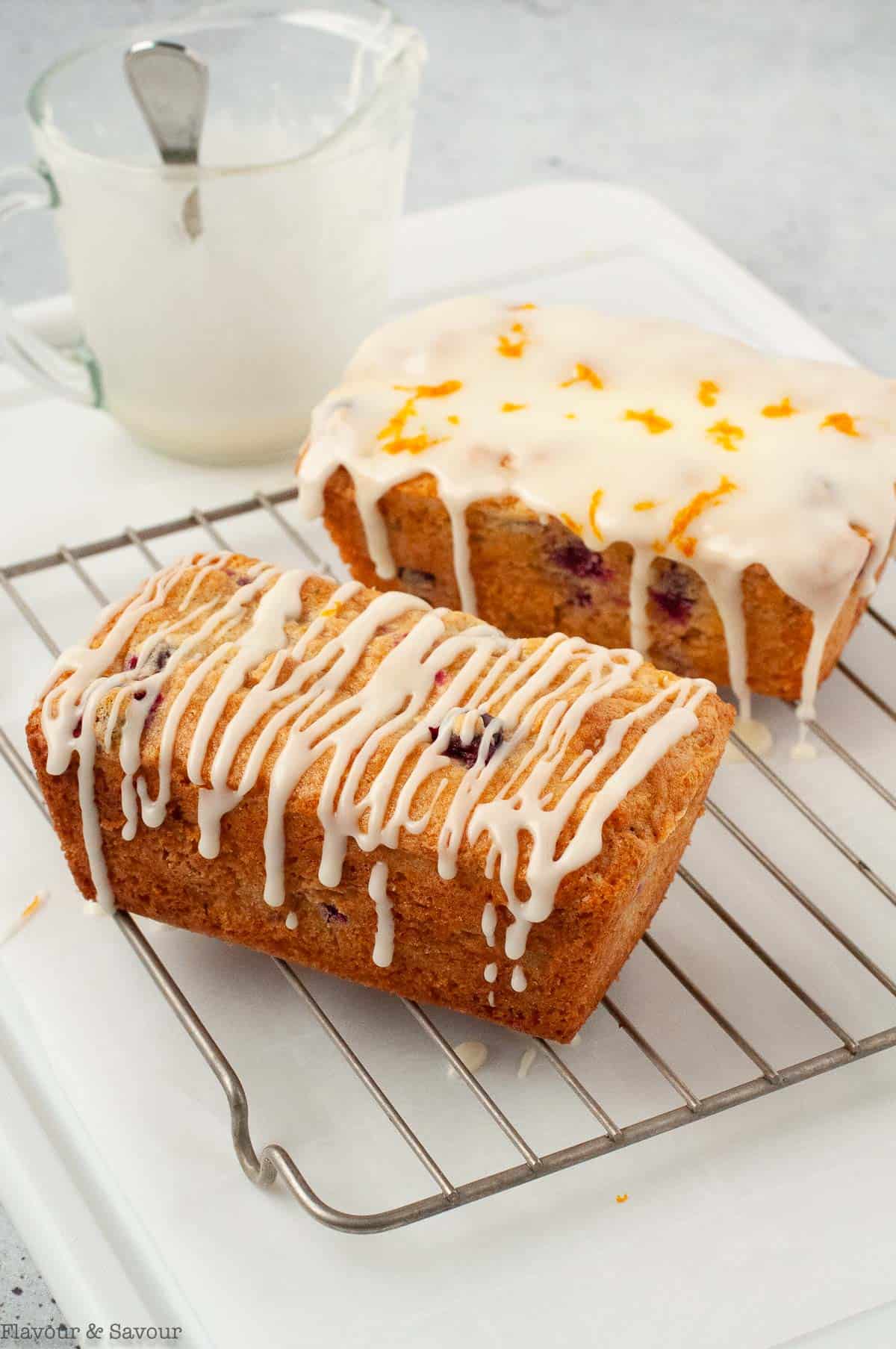 two loaves of cranberry orange bread, one drizzled with glaze and the second completely glazed