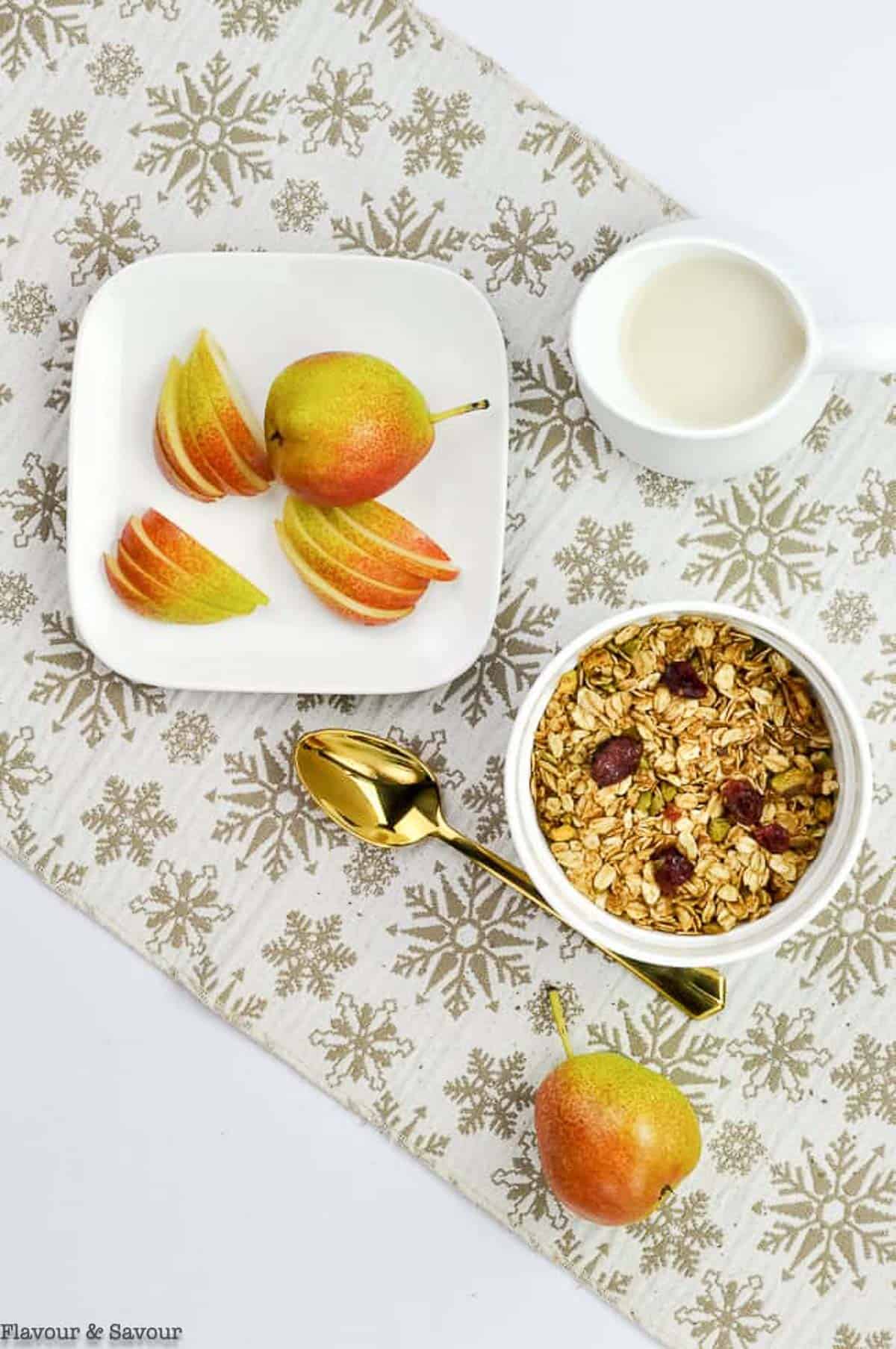 Overhead view of a place setting with gingerbread granola, pears and a pitcher of milk.