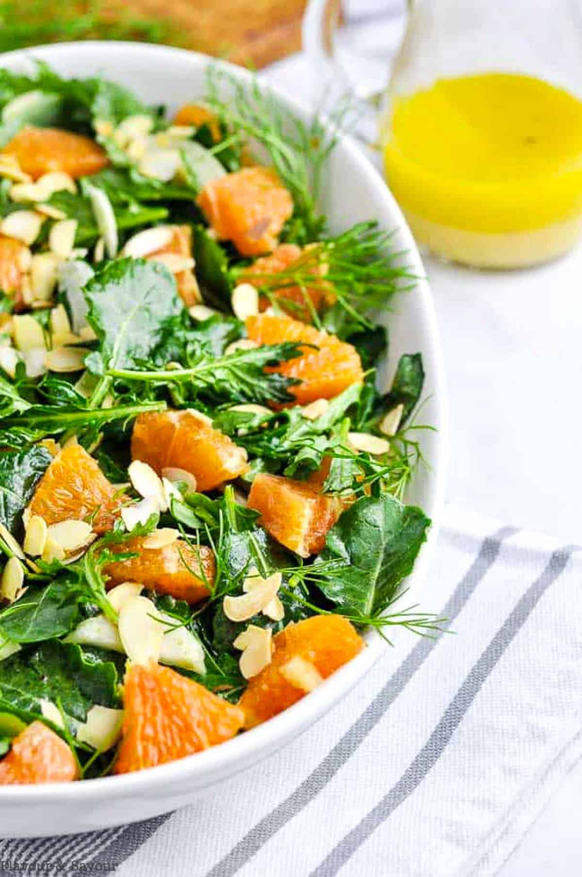 close up view of kale and cara cara orange salad with a pitcher of salad dressing beside.