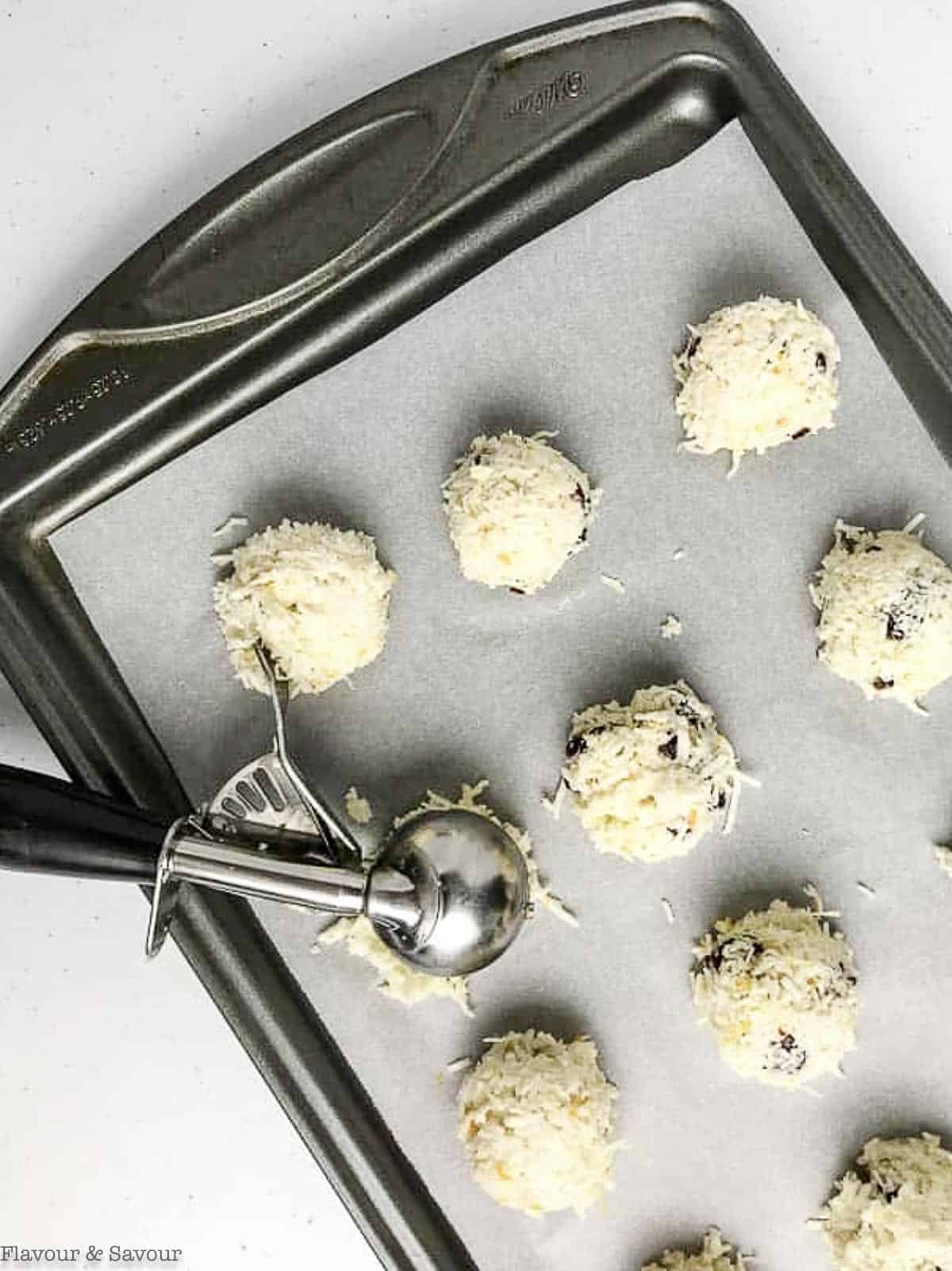 using a cookie scoop to place white chocolate macaroons on a parchment paper lined baking sheet