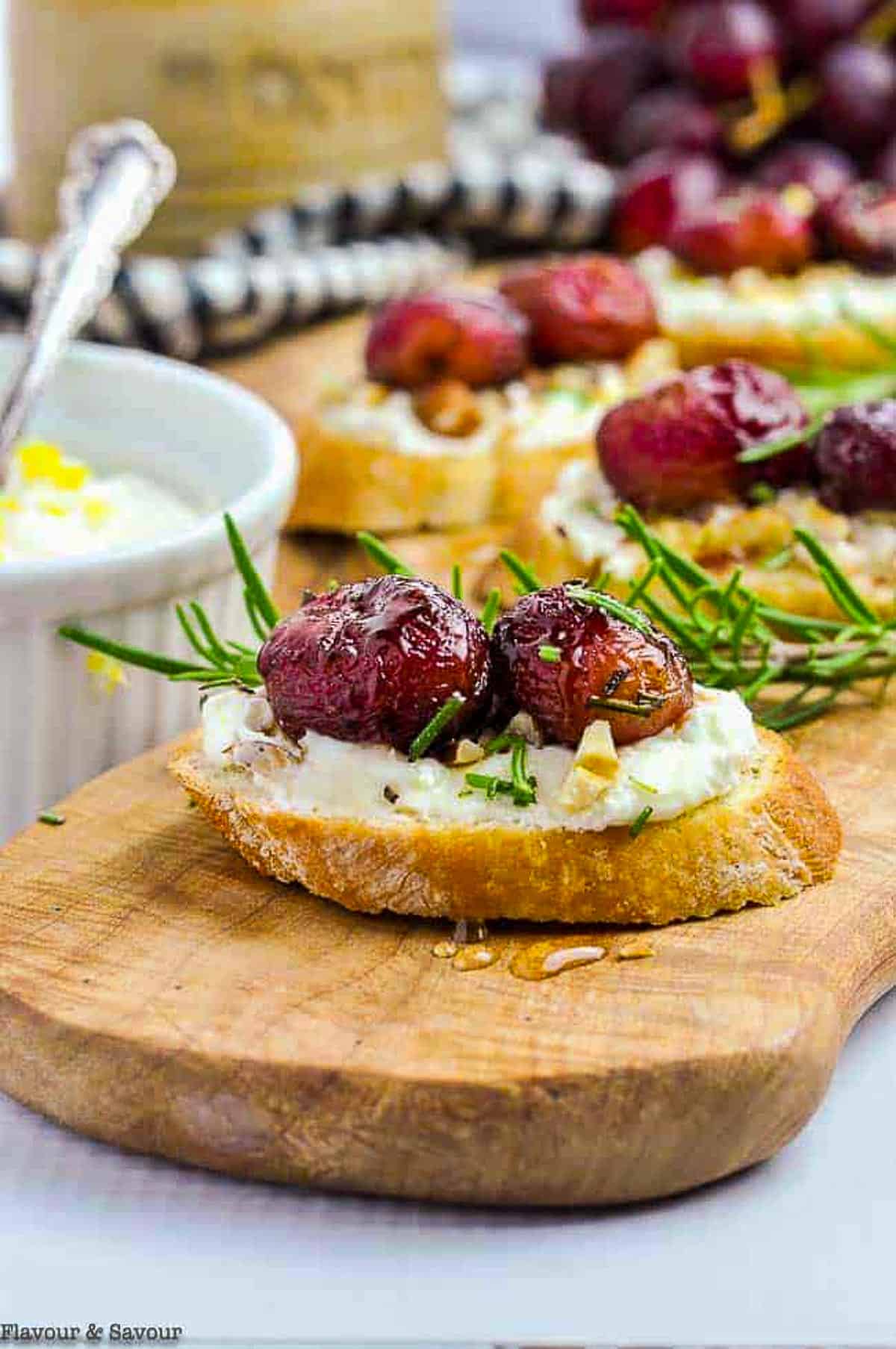 Roasted grape and goat cheese crostini on a serving board with rosemary
