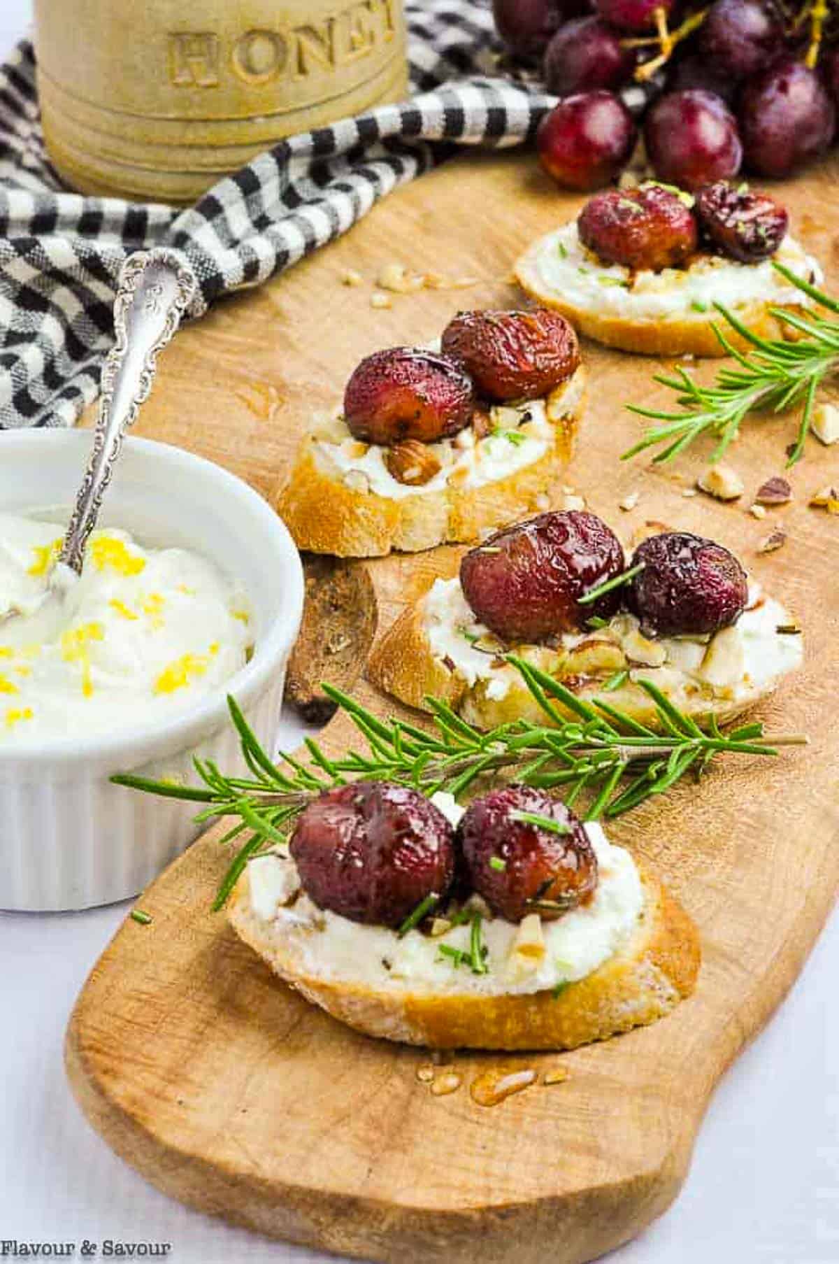 crostini appetizers with goat cheese and roasted grapes with a pot of honey and a bowl of whipped goat cheese