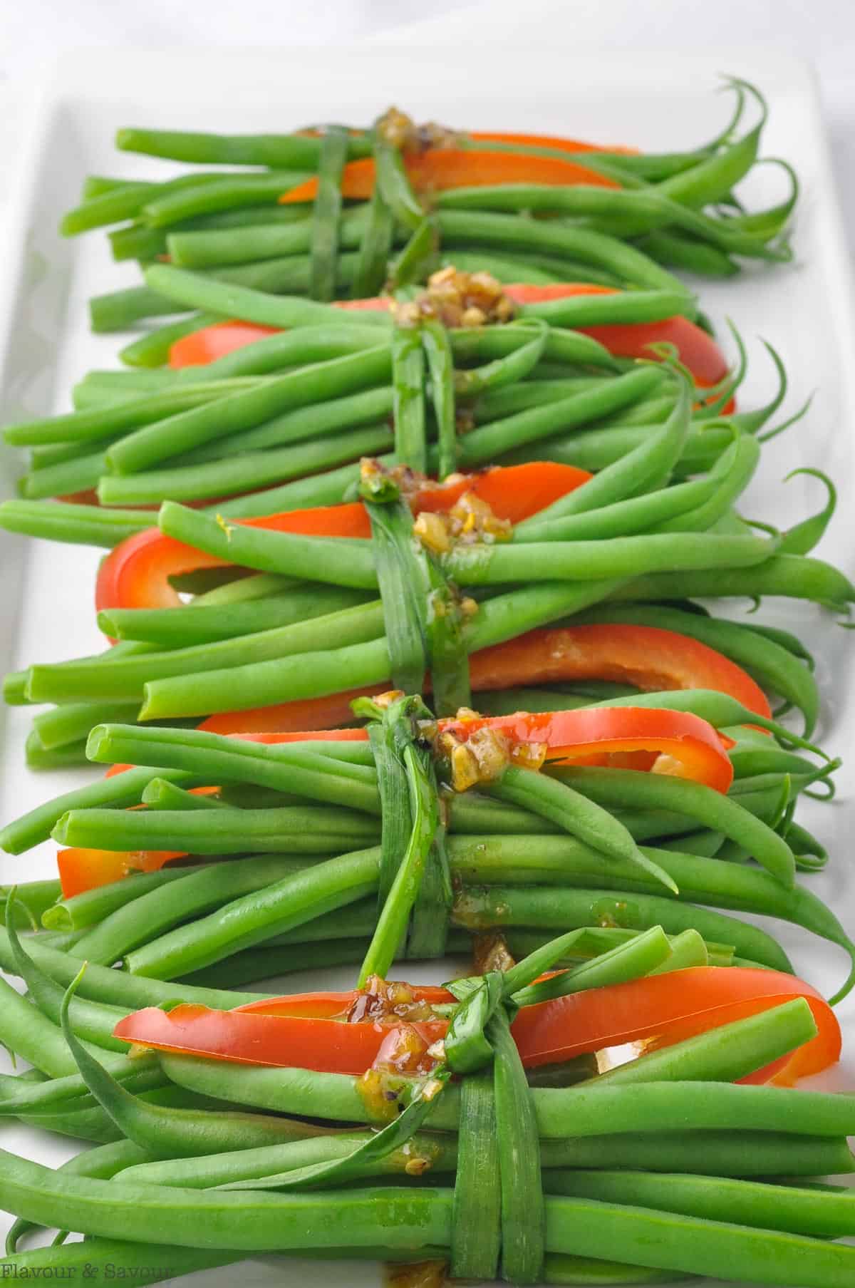 Green bean bundles tied with a chive on a white platter.