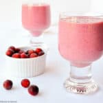 two glasses of cranberry raspberry smoothie with a bowl of frozen cranberries