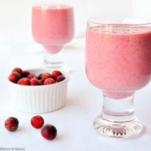 two glasses of cranberry raspberry smoothie with a bowl of frozen cranberries