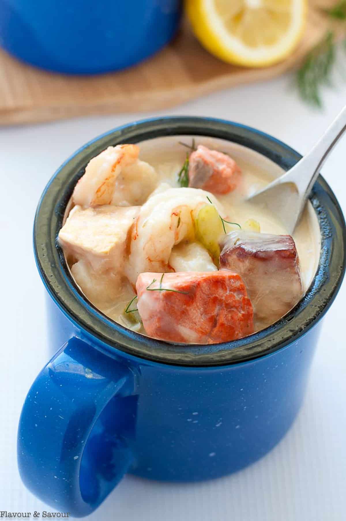 a blue mug filled with seafood chowder made with salmon, shrimp, halibut and more