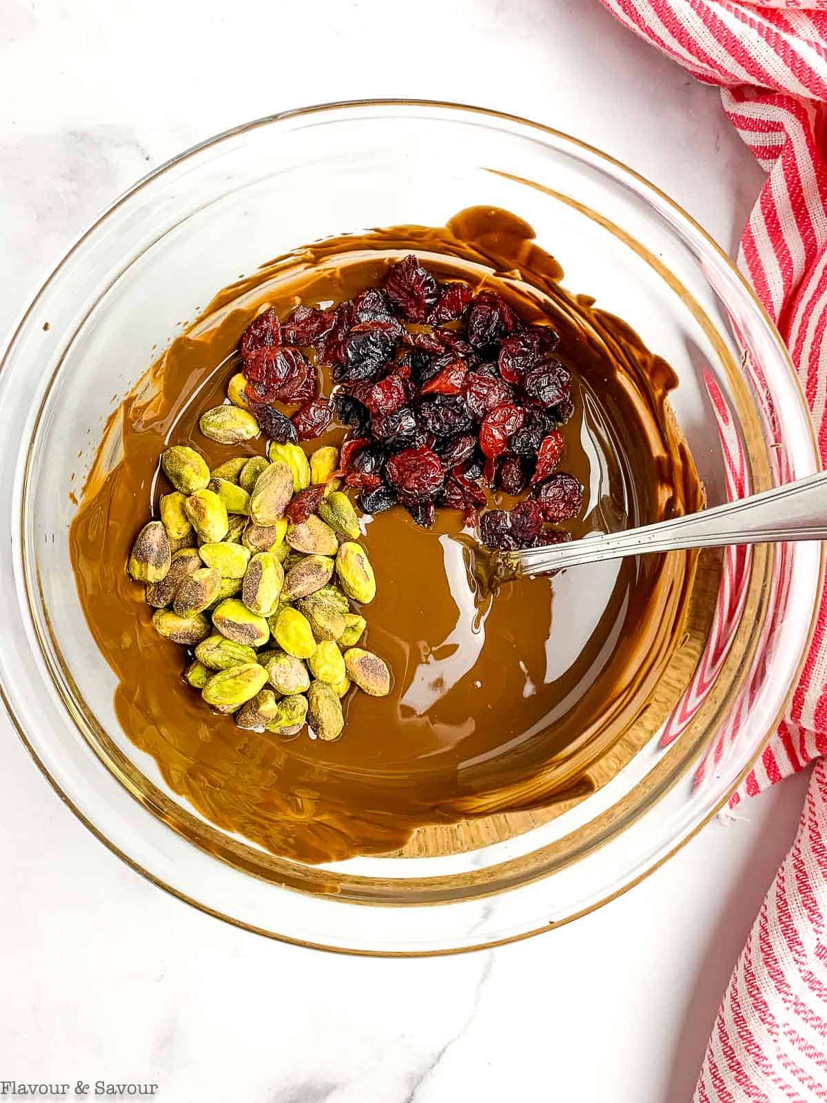 adding dried cranberries and pistachios to melted chocolate