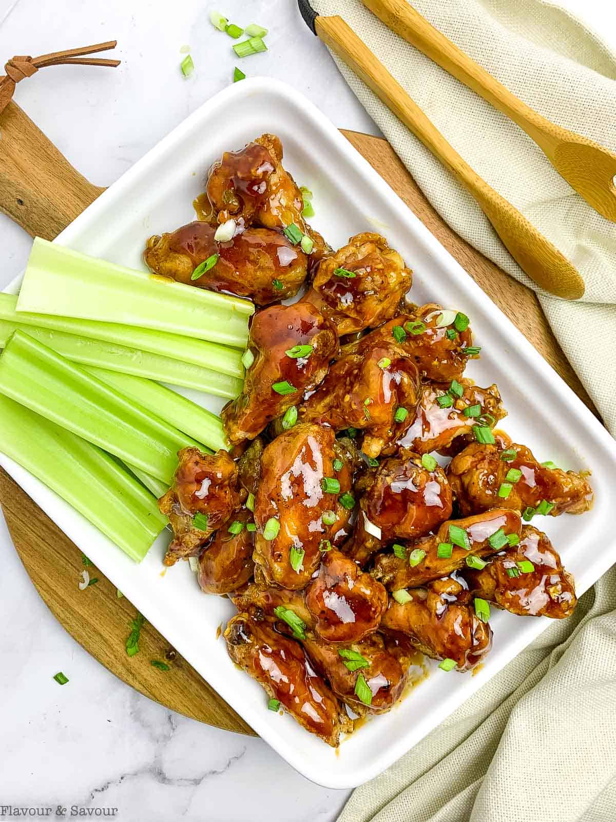 A platter of air fryer honey garlic chicken wingsgarnished with green onion and served with celery sticks.