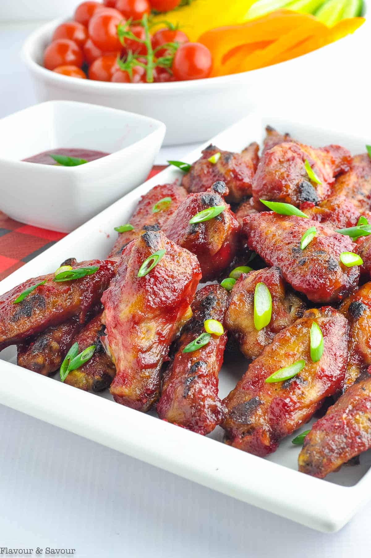 A platter of cranberry glazed wings with chili sauce, garnished with thinly sliced green onions.