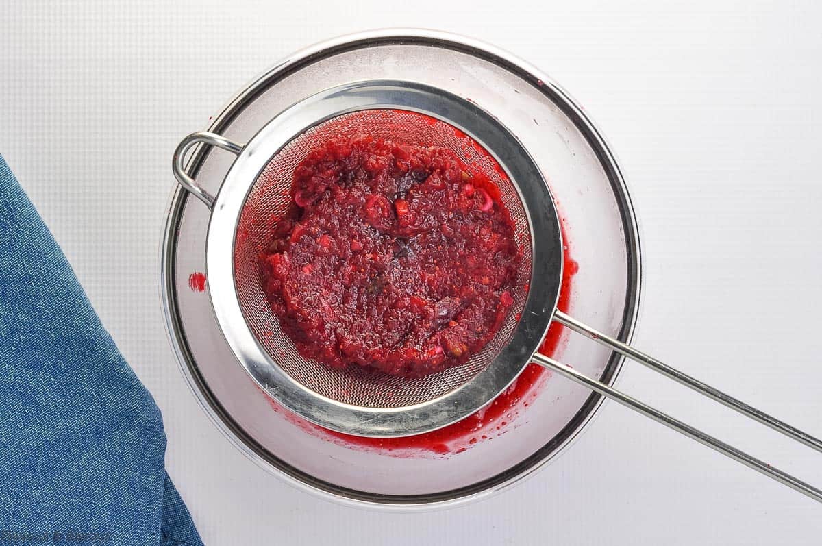 Straining cranberries through a sieve to make cranberry glaze.