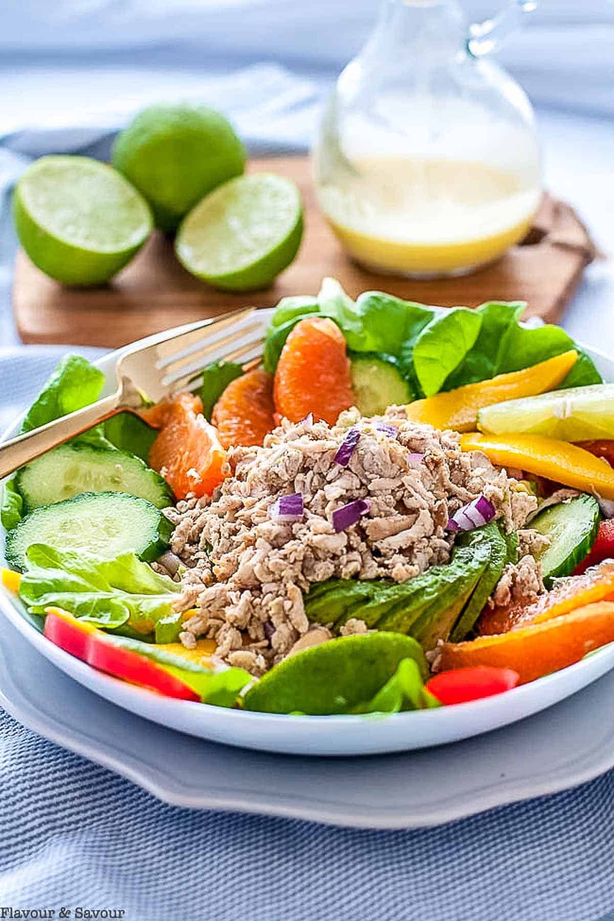 Jerk chicken salad in a bowl with a fork and a pitcher of dressing nearby.